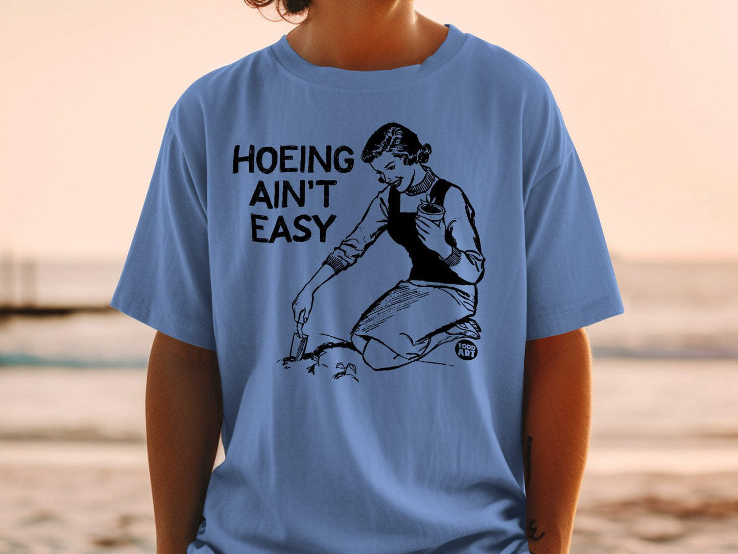 Black and white illustration on a blue t-shirt: "Hoeing Ain't Easy".