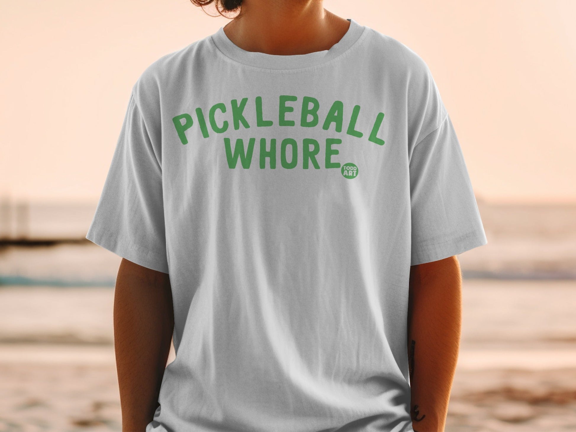 White t-shirt with "PICKLEBALL WHORE" and "1000 ART" in green text.