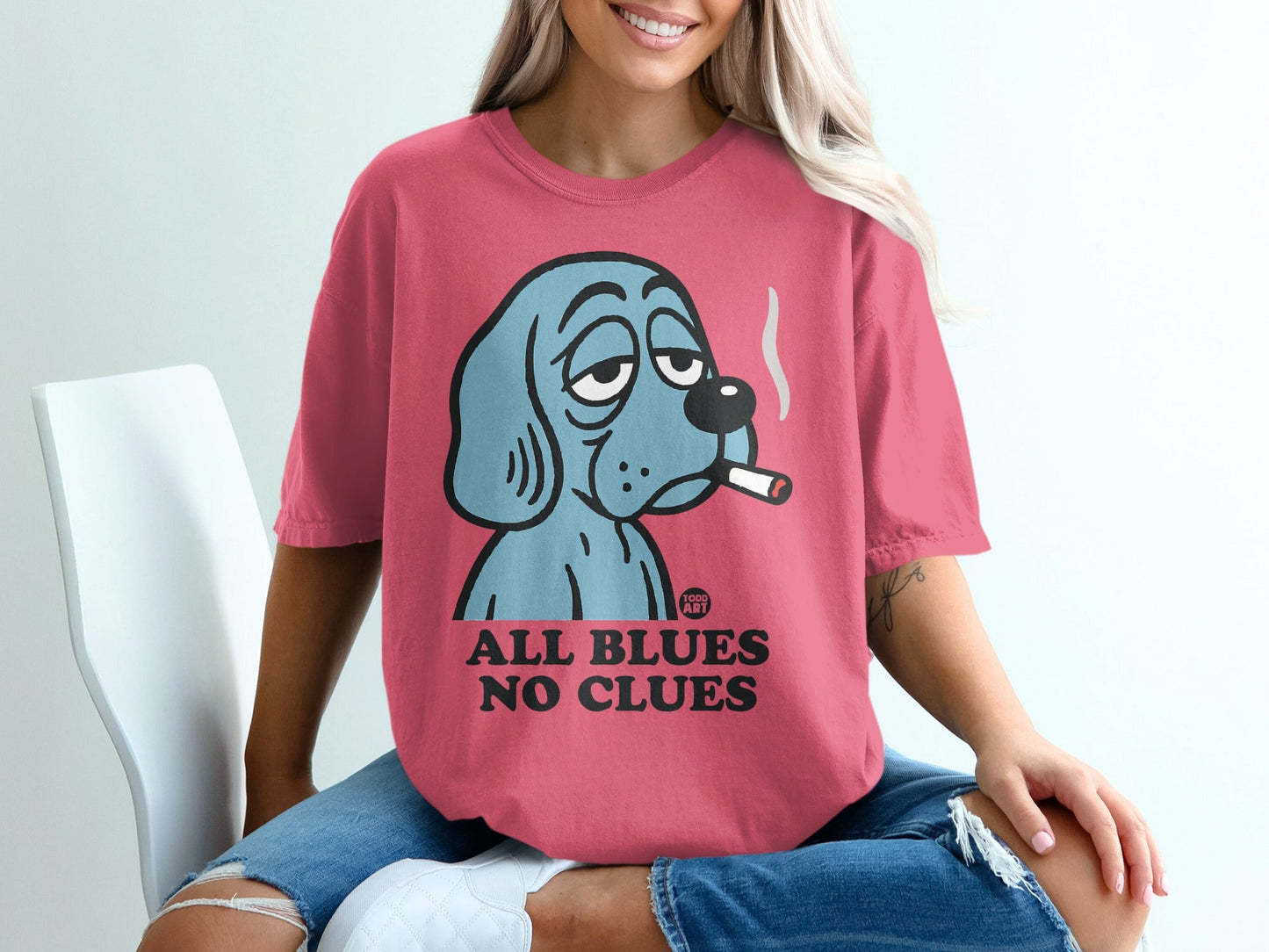 Pink t-shirt with cartoon blue dog smoking a cigarette, text "ALL BLUES NO CLUES".