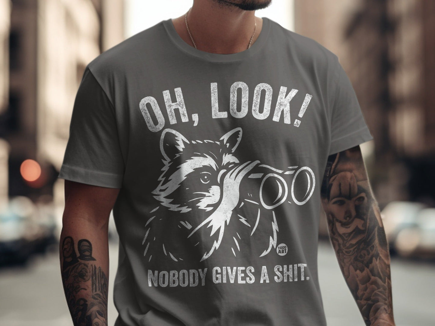 Grey t-shirt with raccoon looking through binoculars, text "OH, LOOK! NOBODY GIVES A SHIT."