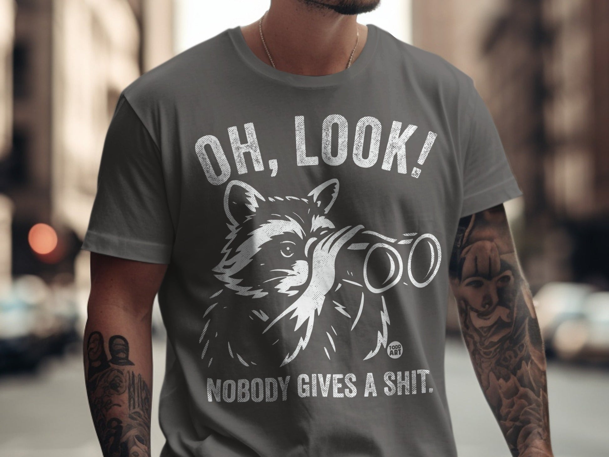 Grey t-shirt with raccoon looking through binoculars, text "OH, LOOK! NOBODY GIVES A SHIT."