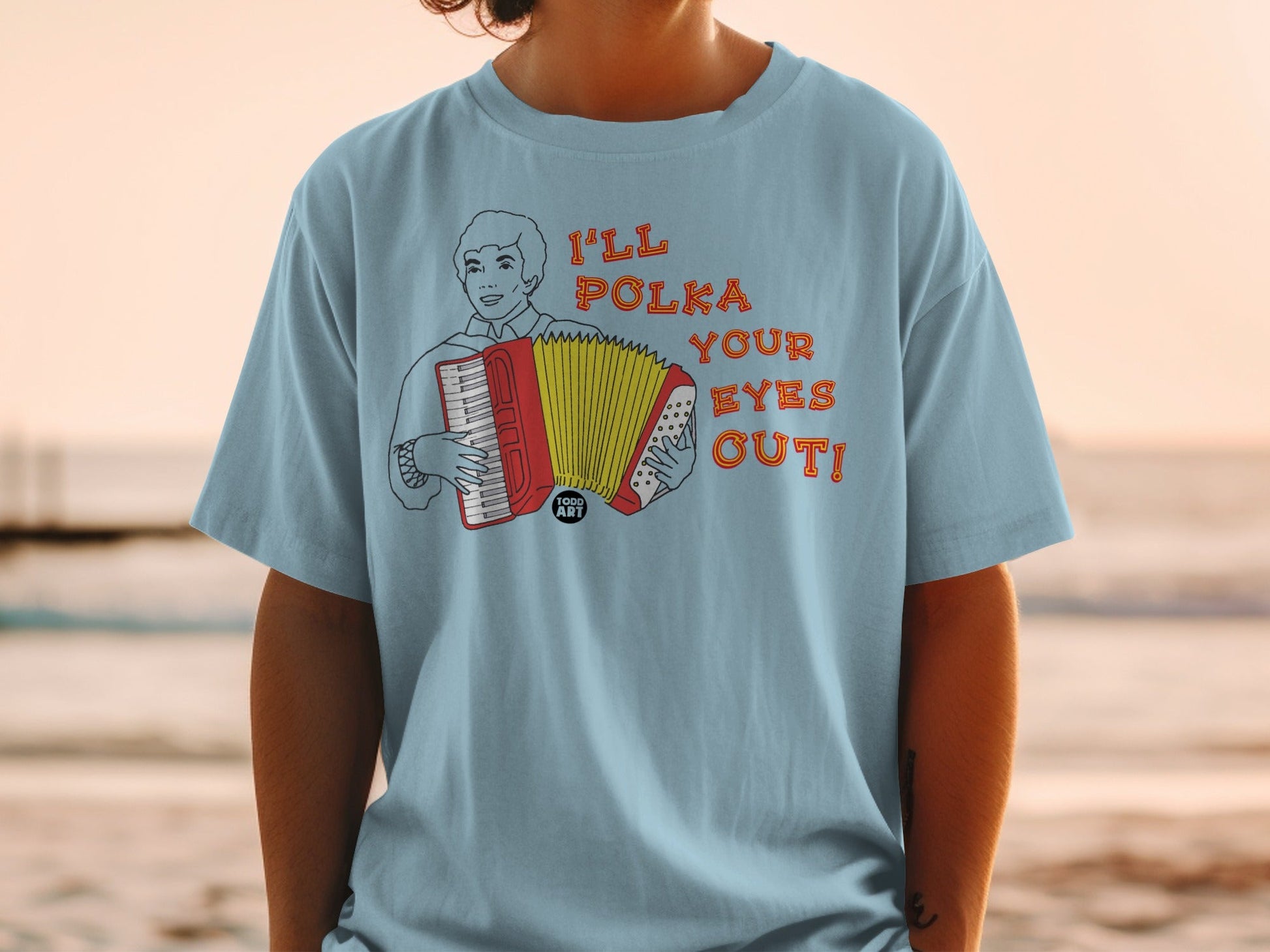 Light blue t-shirt with a cartoon man playing an accordion, text "I'LL POLKA YOUR EYES OUT!".