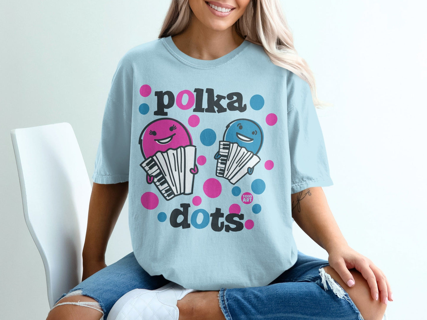 Light blue t-shirt with pink and blue polka dot text and cartoon accordions.