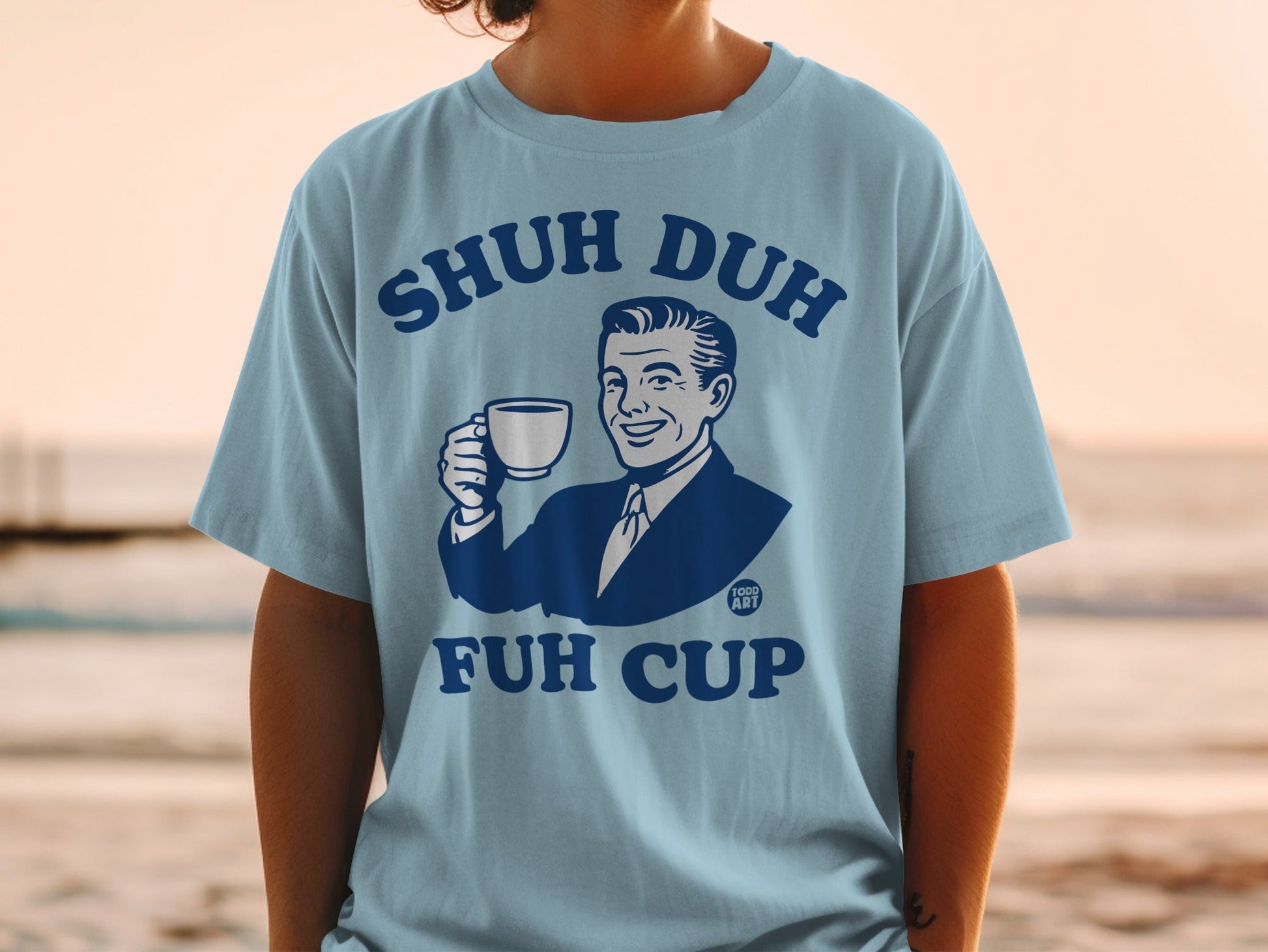 Light blue t-shirt with cartoon man holding a cup, text reads "SHUH DUH FUH CUP".