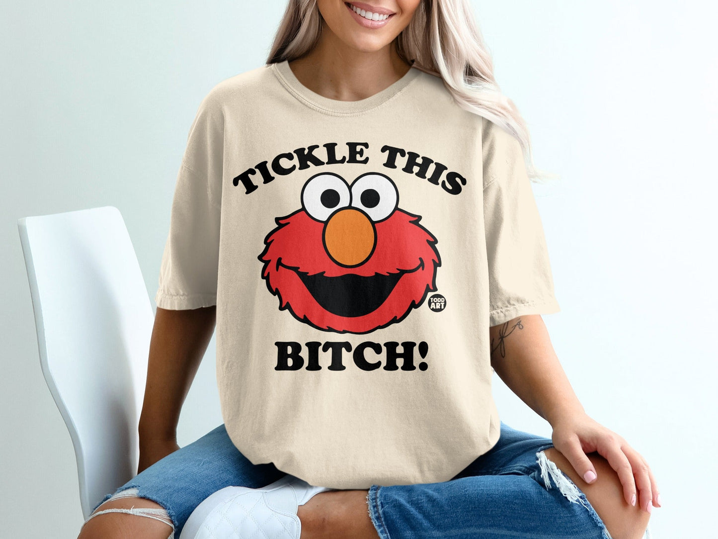 Elmo character with text "Tickle This Bitch!" on a beige t-shirt.