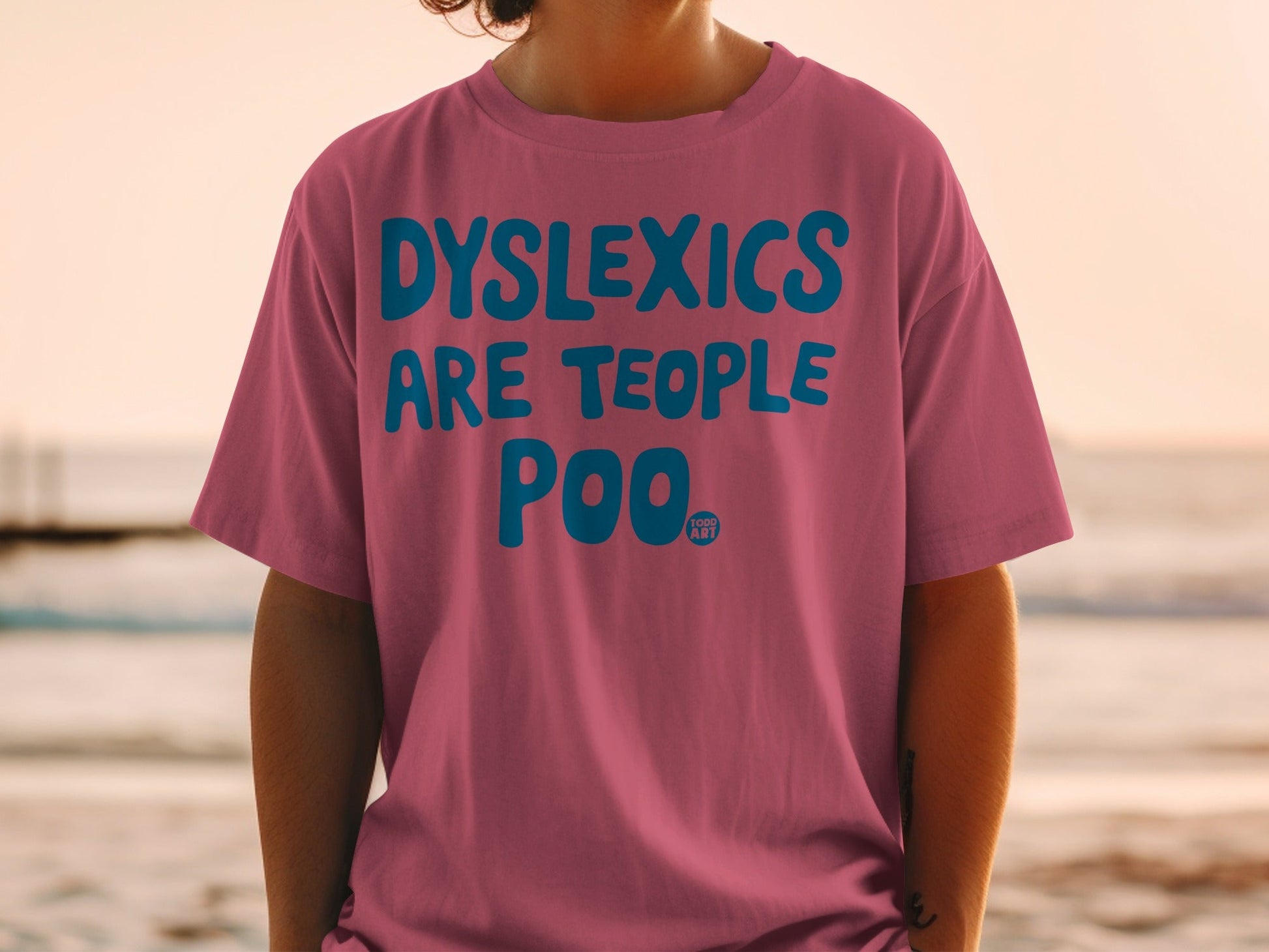 Pink t-shirt with bold blue text reading "DYSLEXICS ARE PEOPLE TOO" and a small logo.