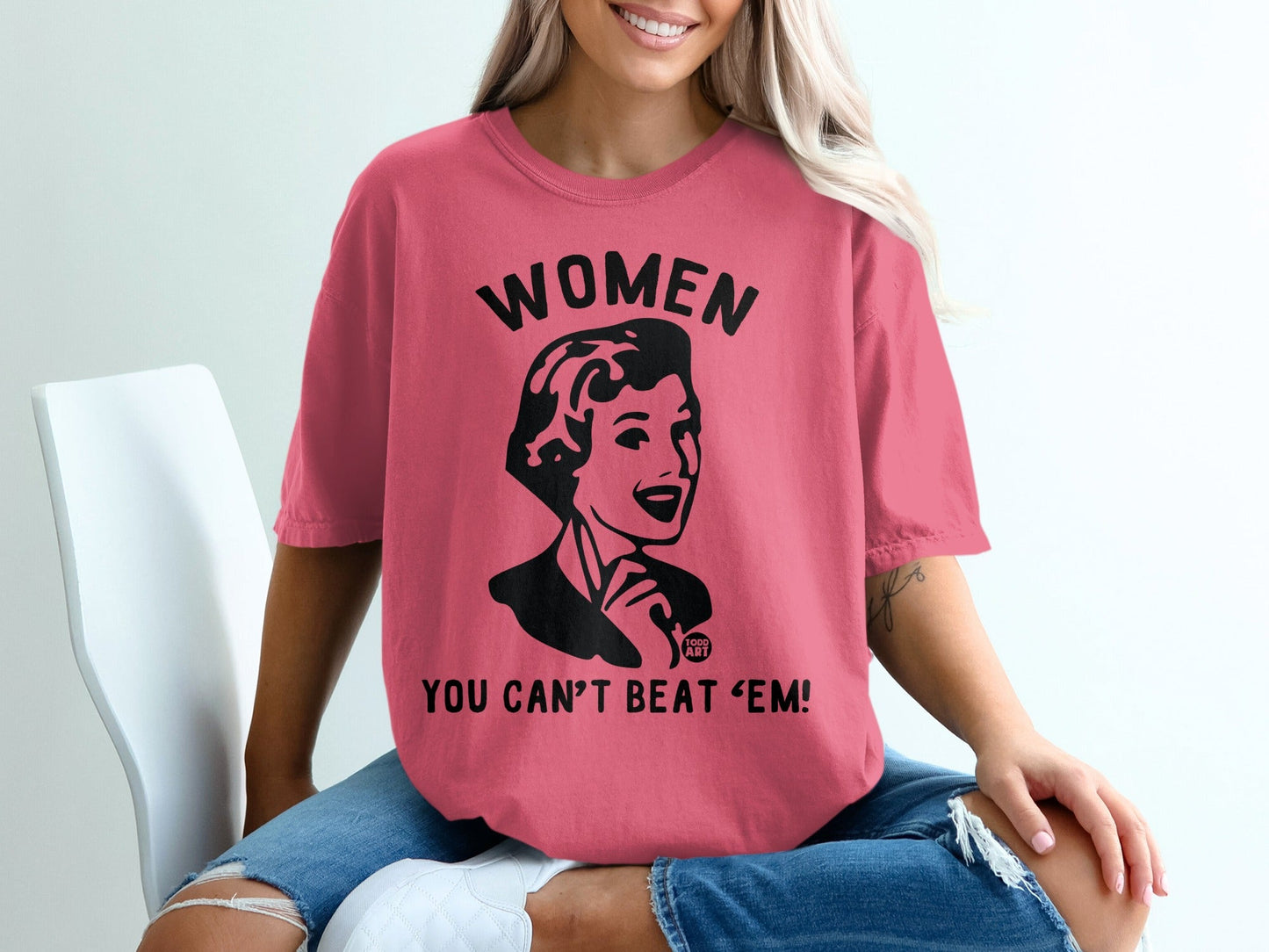 Pink t-shirt with retro woman graphic and "WOMEN YOU CAN'T BEAT 'EM!" text.