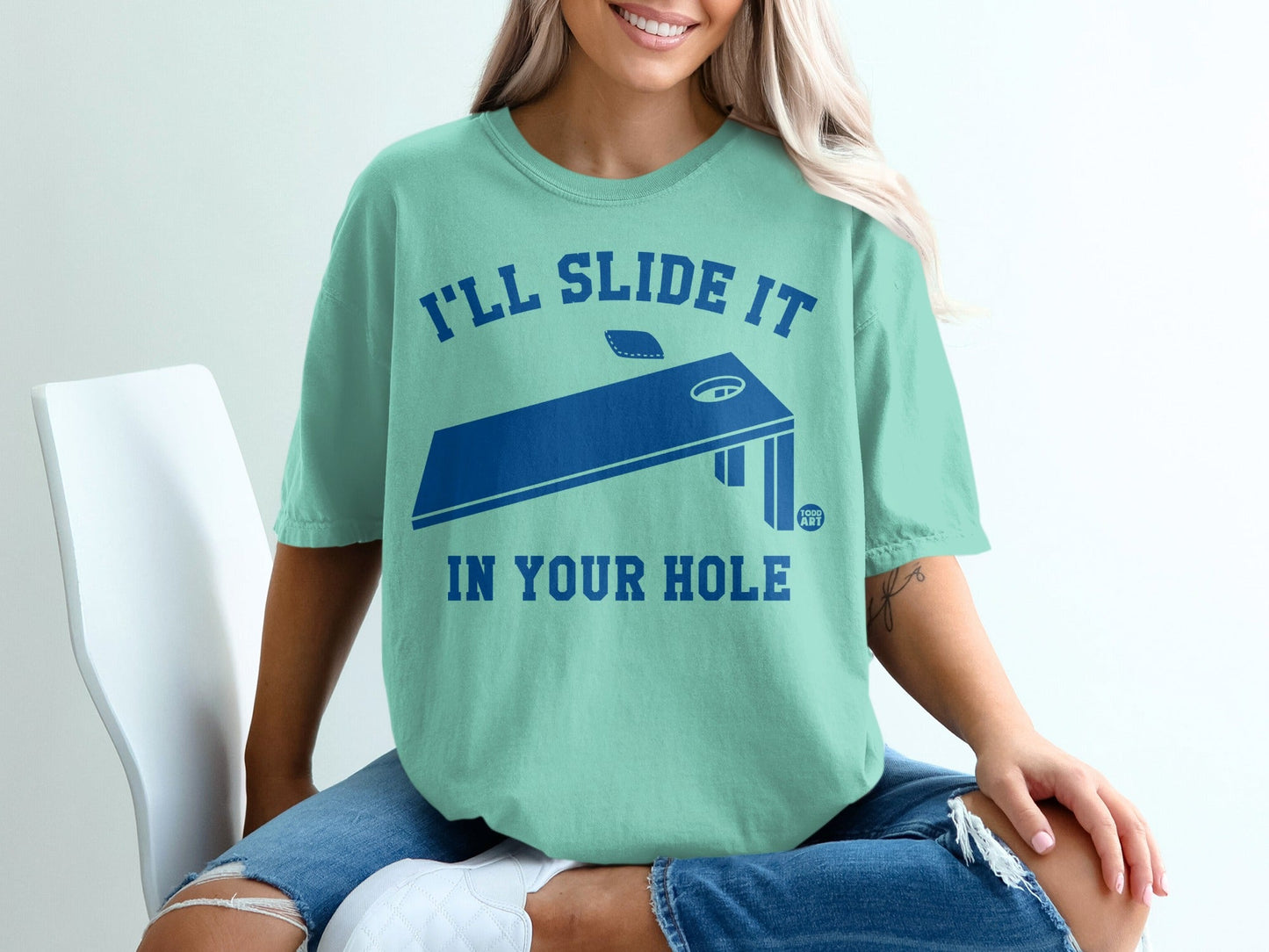 Teal t-shirt with "I'll slide it in your hole" and cornhole board design.