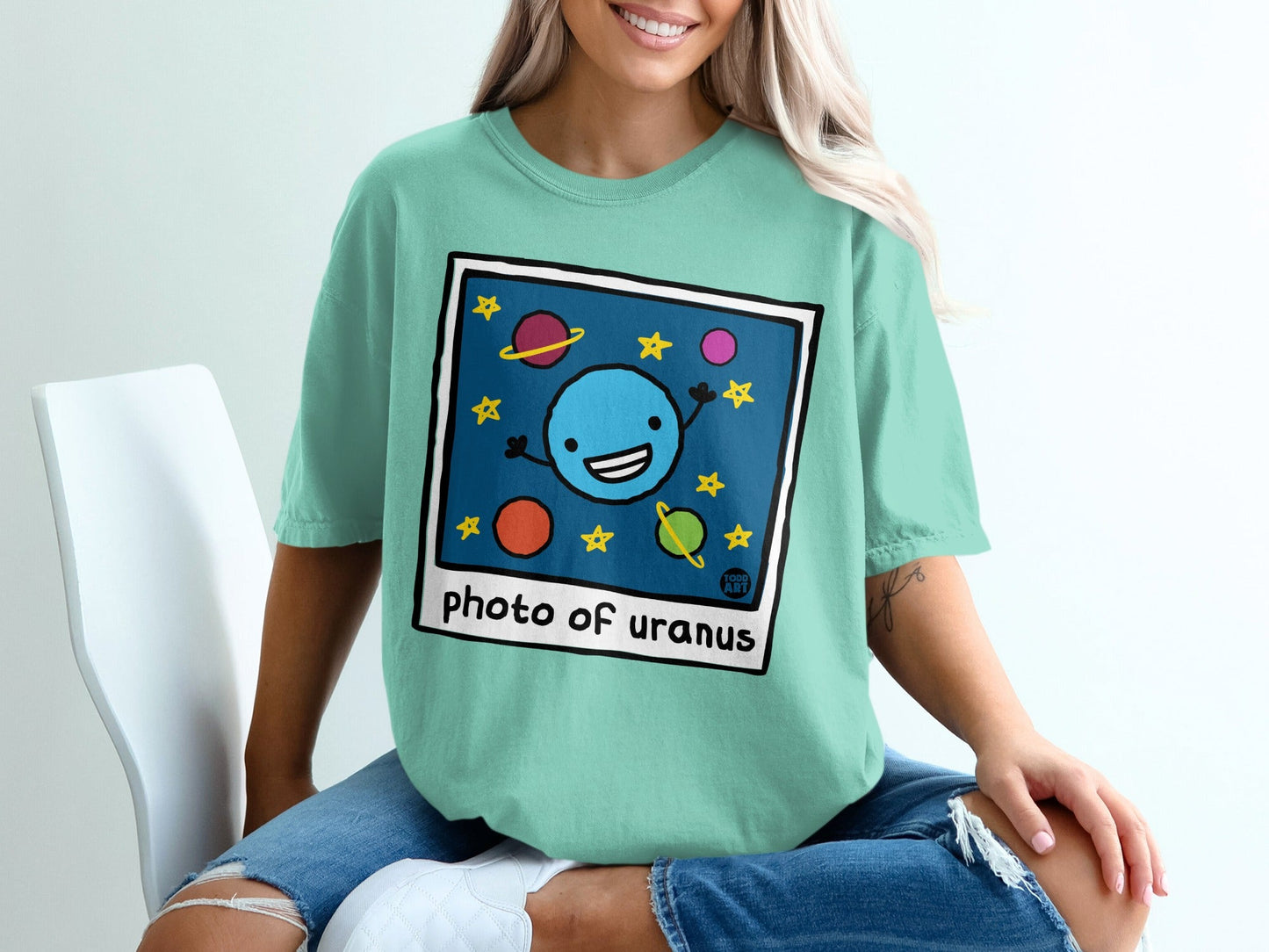 Illustration of cartoon Uranus with stars and planets on a teal t-shirt.