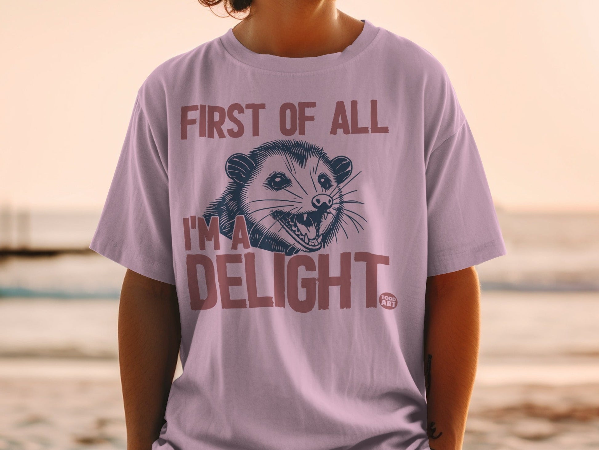Pink t-shirt with a possum graphic and text "First of all I'm a delight."