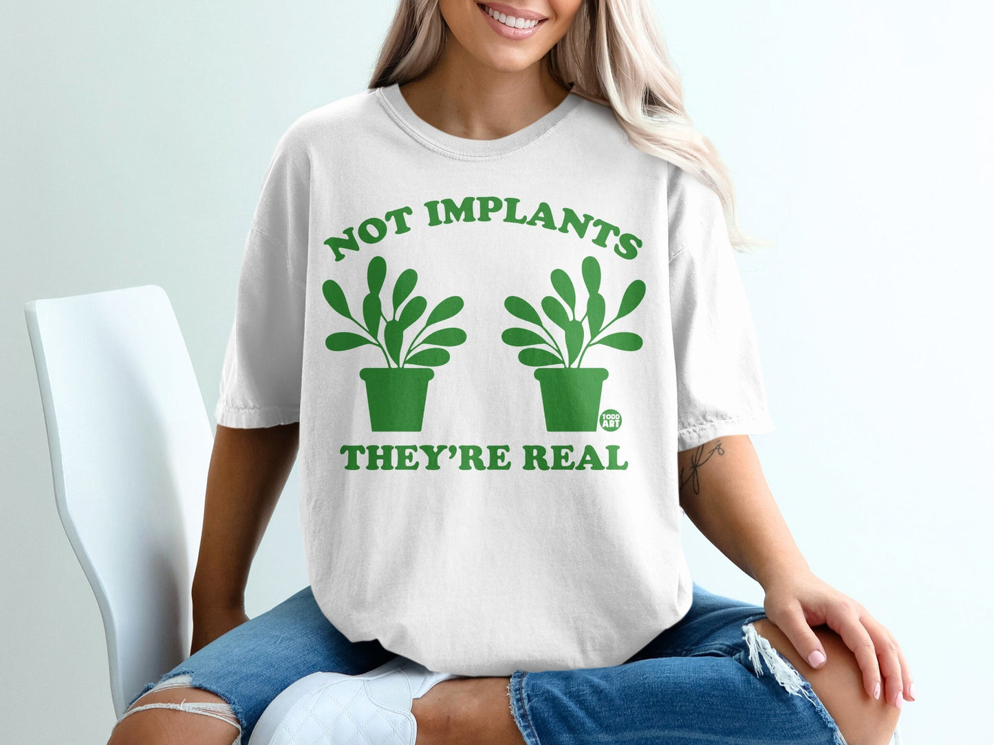 White t-shirt with green potted plants and text "NOT IMPLANTS THEY'RE REAL".