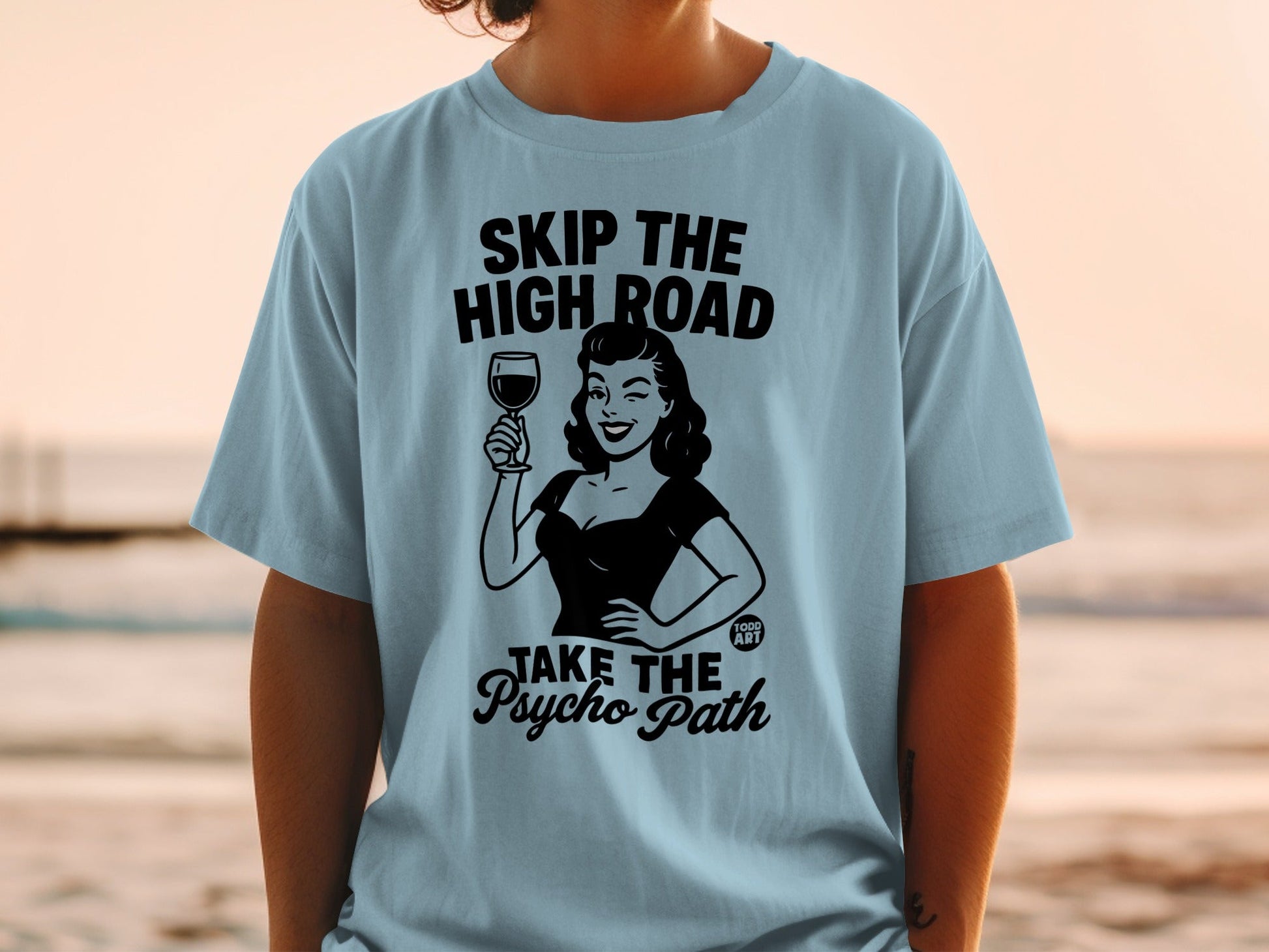 Light blue t-shirt with black graphic of woman holding wine, "SKIP THE HIGH ROAD TAKE THE PSYCHO PATH".