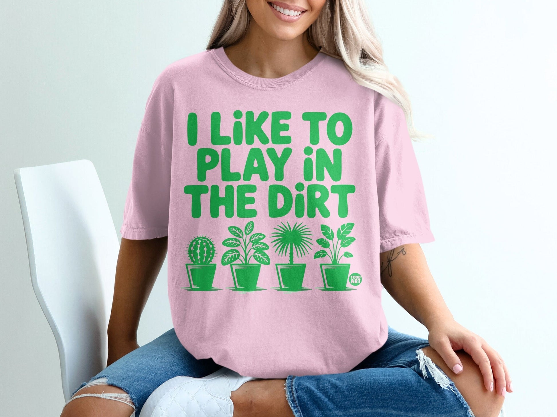 Pink t-shirt with green text "I LIKE TO PLAY IN THE DIRT" and potted plants.