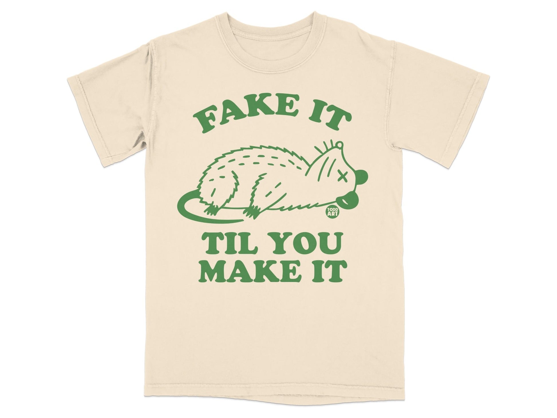 Beige t-shirt with "FAKE IT TIL YOU MAKE IT" and a dead opossum graphic.
