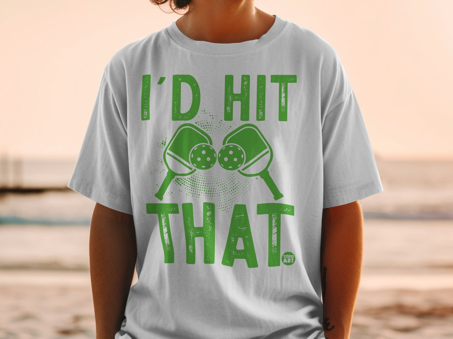 White t-shirt with green text "I'D HIT THAT" and pickleball paddles and balls.