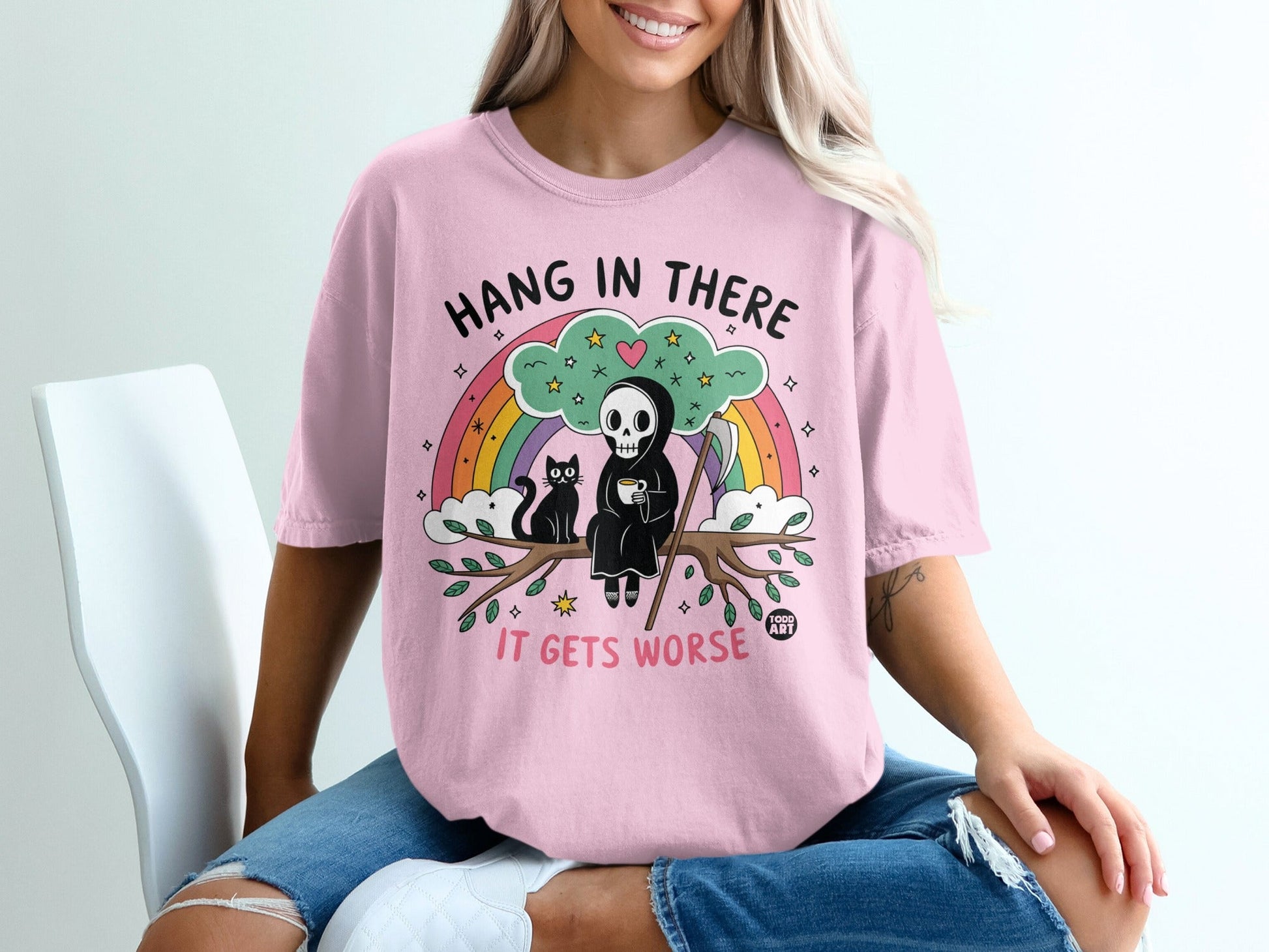 Pink t-shirt with Grim Reaper, cat, and rainbow graphic that says "Hang in there it gets worse".