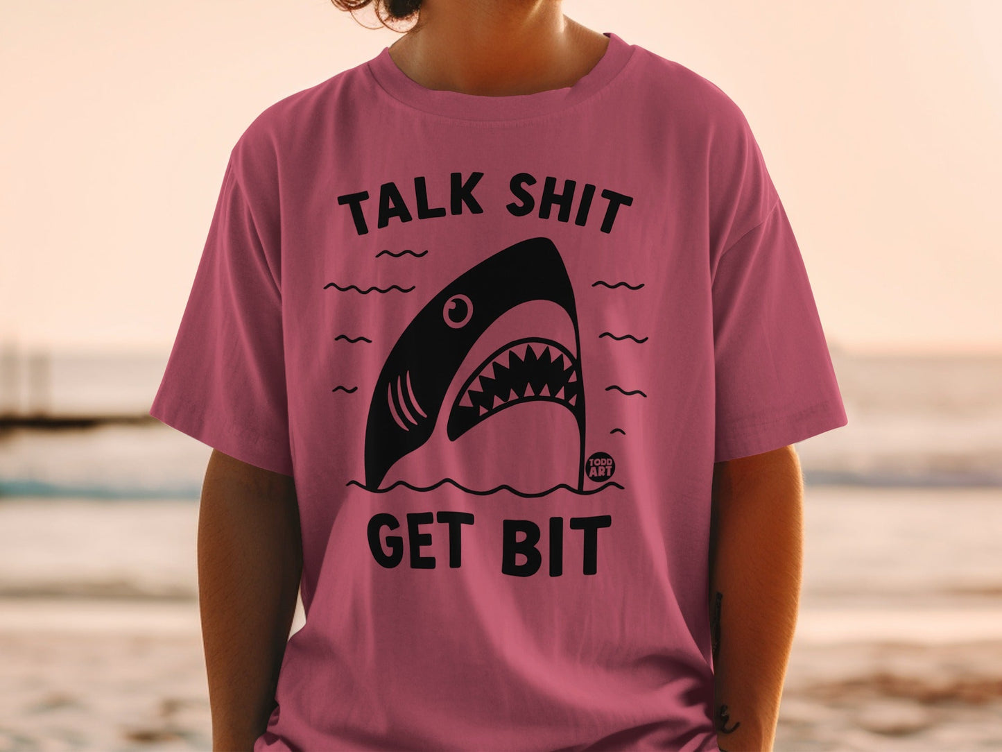 Pink t-shirt with black shark graphic and "TALK SHIT GET BIT" text.