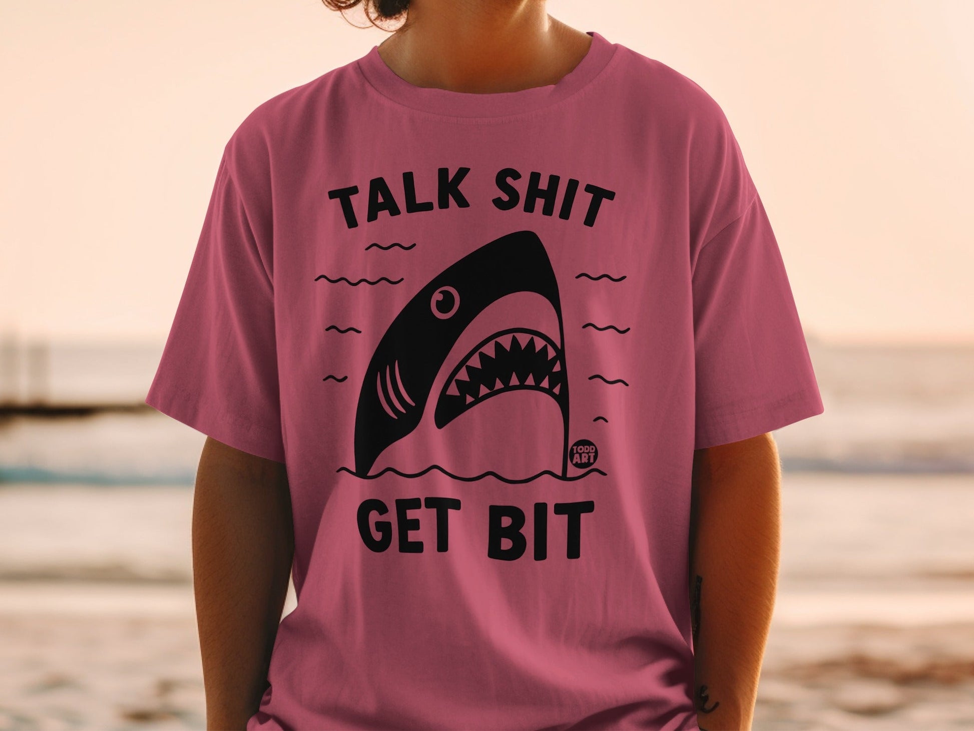 Pink t-shirt with black shark graphic and "TALK SHIT GET BIT" text.
