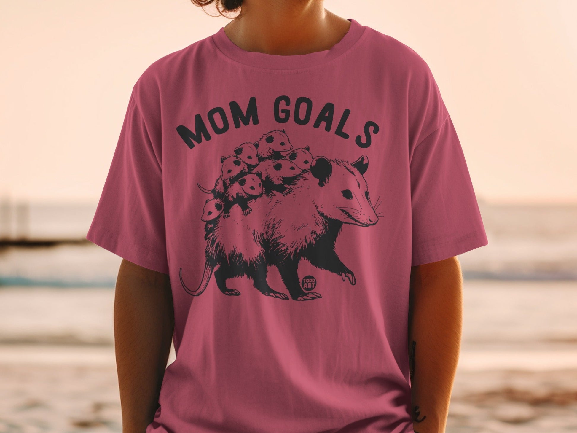 T-shirt with "Mom Goals" text and opossum with babies illustration.