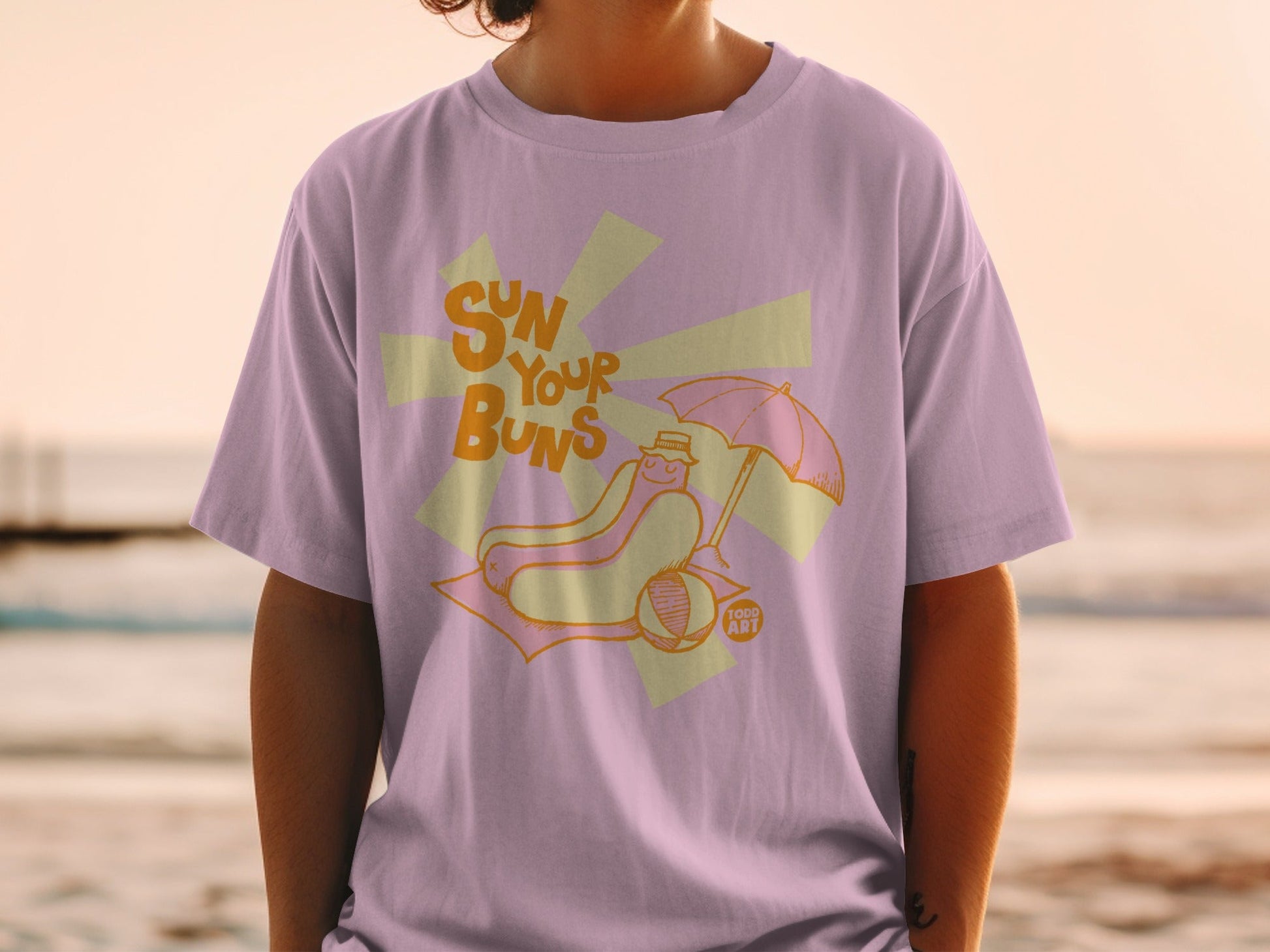 Hot dog on a beach blanket under an umbrella, text reads "SUN YOUR BUNS".