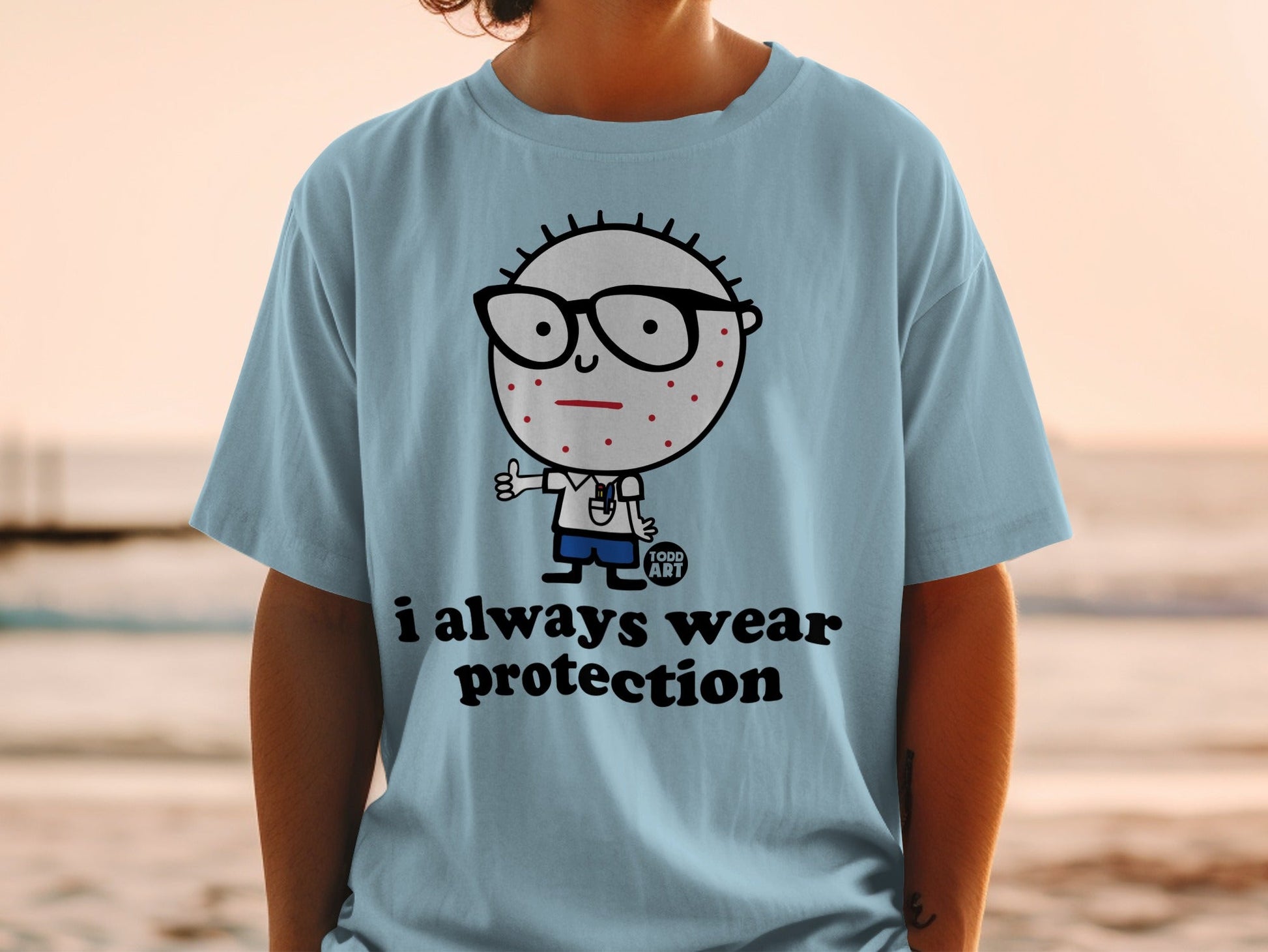 Light blue t-shirt with cartoon character, glasses, and text "i always wear protection."