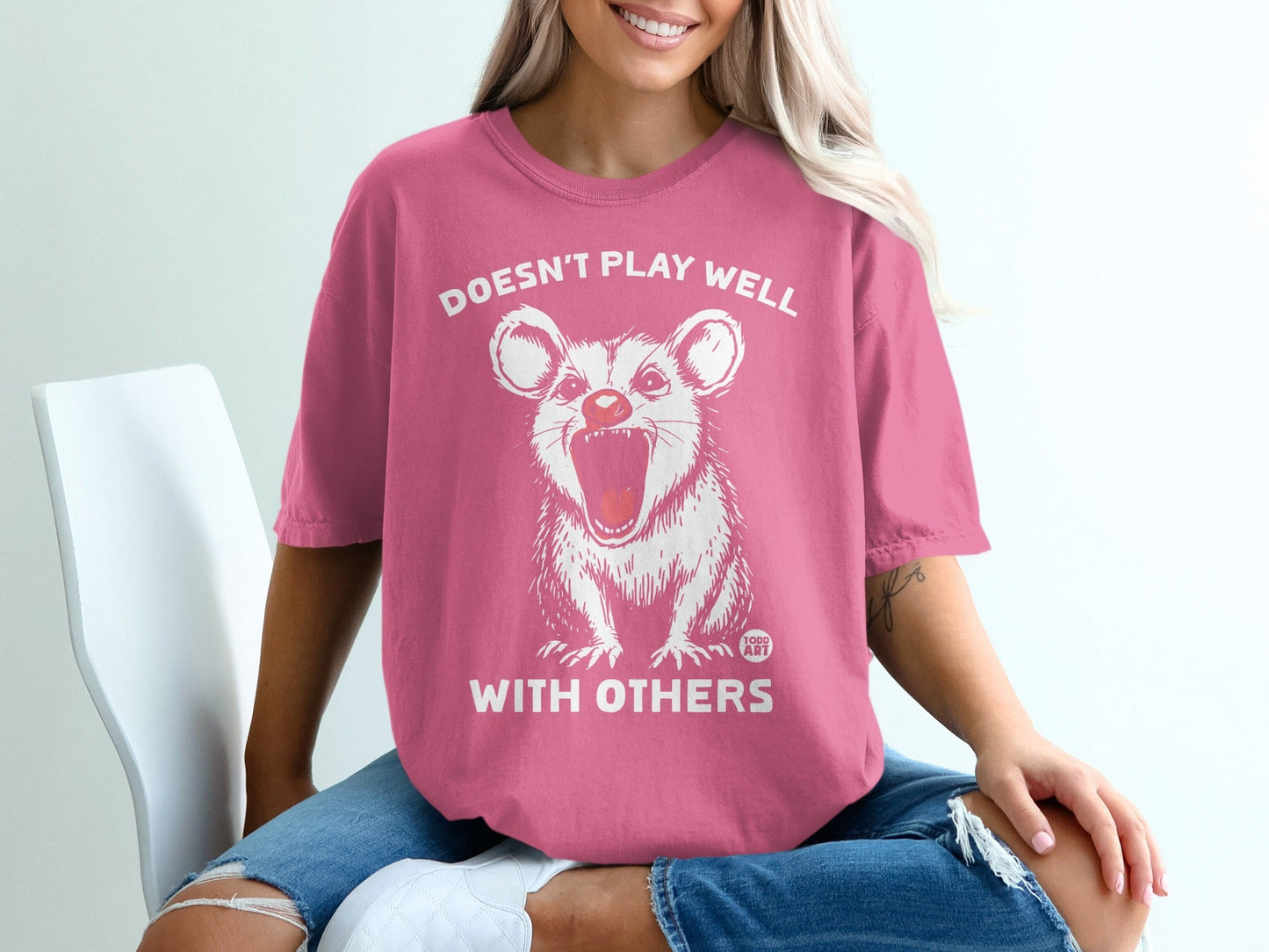 Pink t-shirt with opossum graphic and text "Doesn't play well with others".