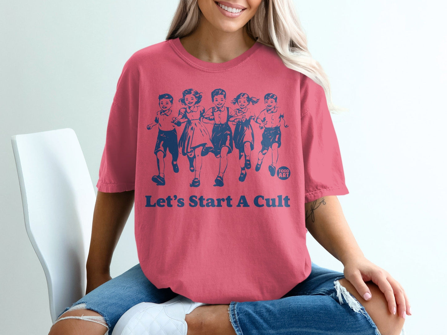 Pink t-shirt with graphic of running children and text "LET'S START A CULT".