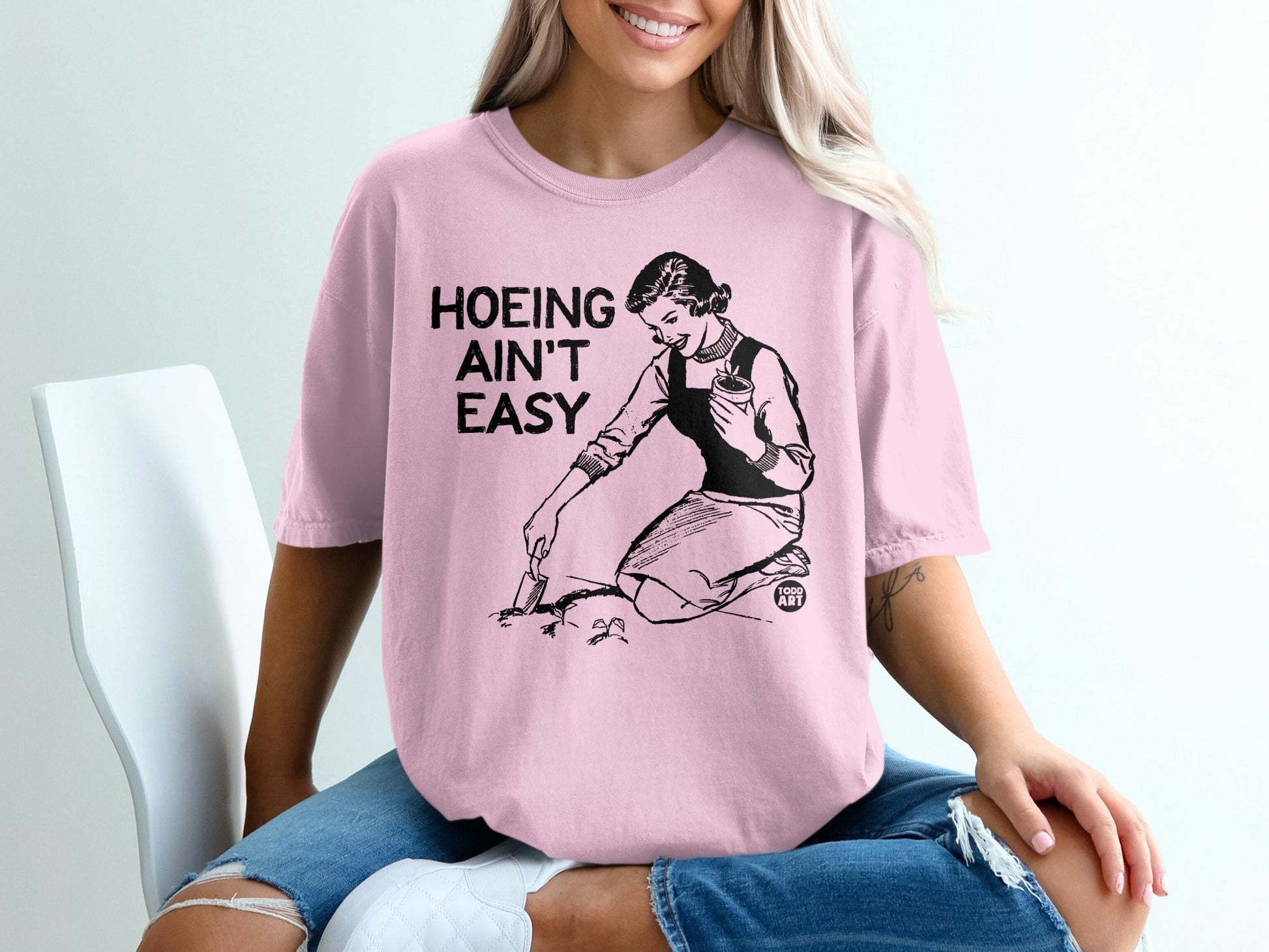 Pink t-shirt with "Hoeing Ain't Easy" text and woman gardening illustration.