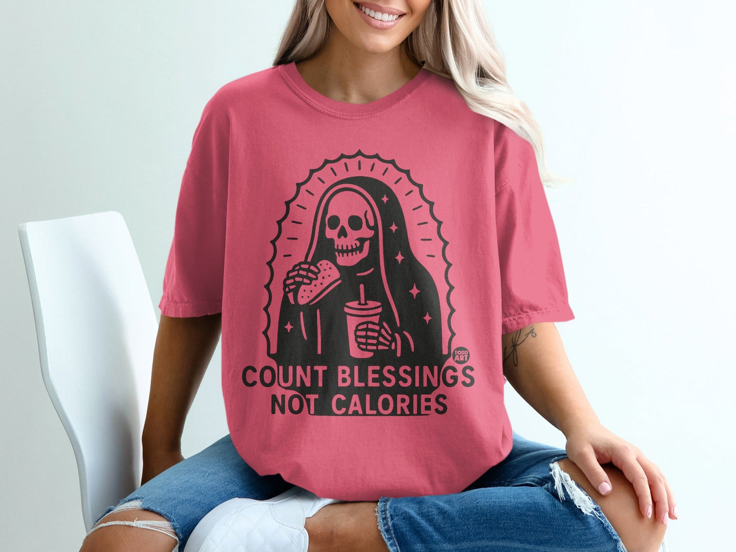 Pink t-shirt with skeleton holding a burger and drink, text "COUNT BLESSINGS NOT CALORIES".