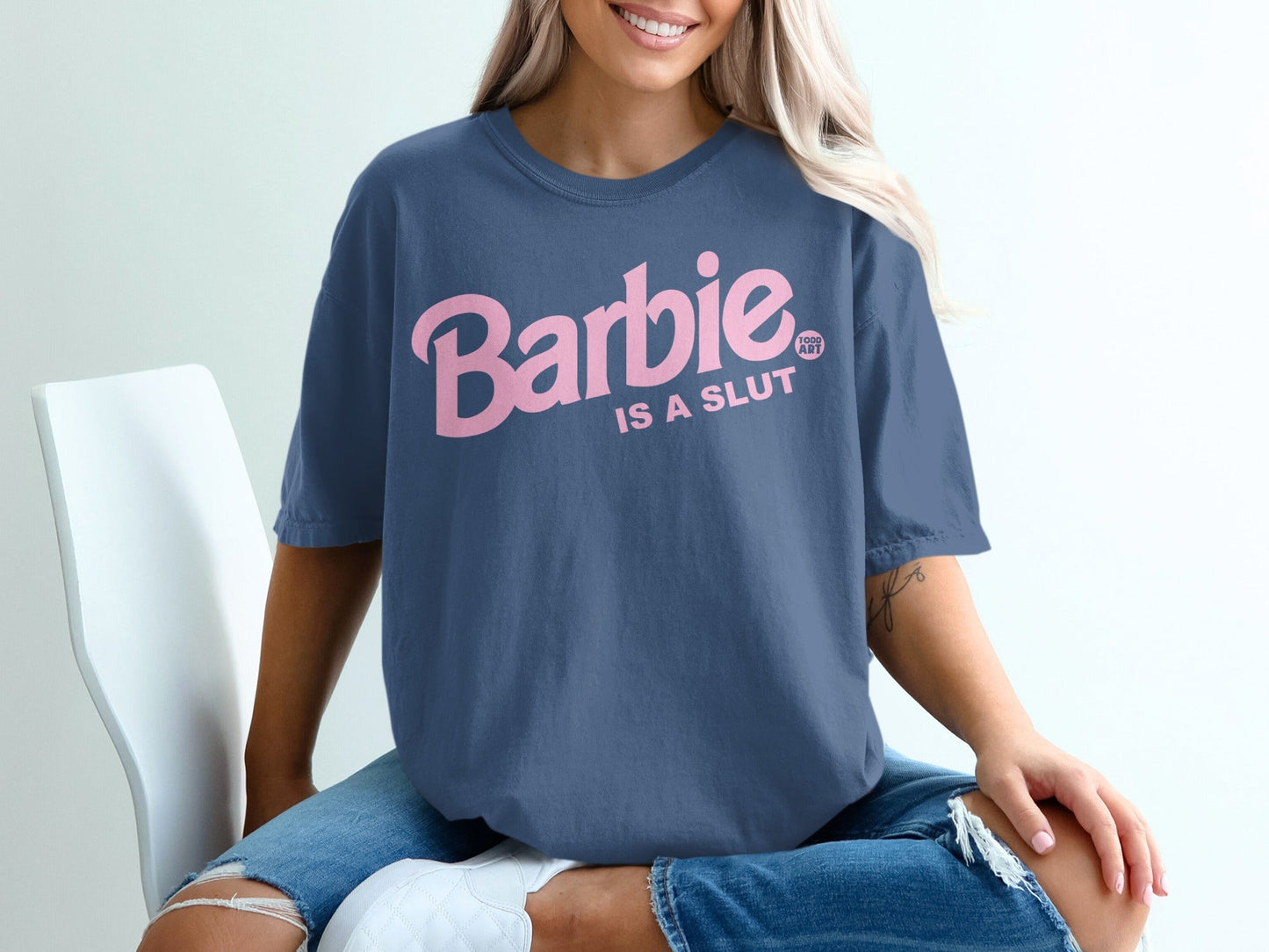Navy t-shirt with pink "Barbie is a slut" graphic, worn by a seated woman.
