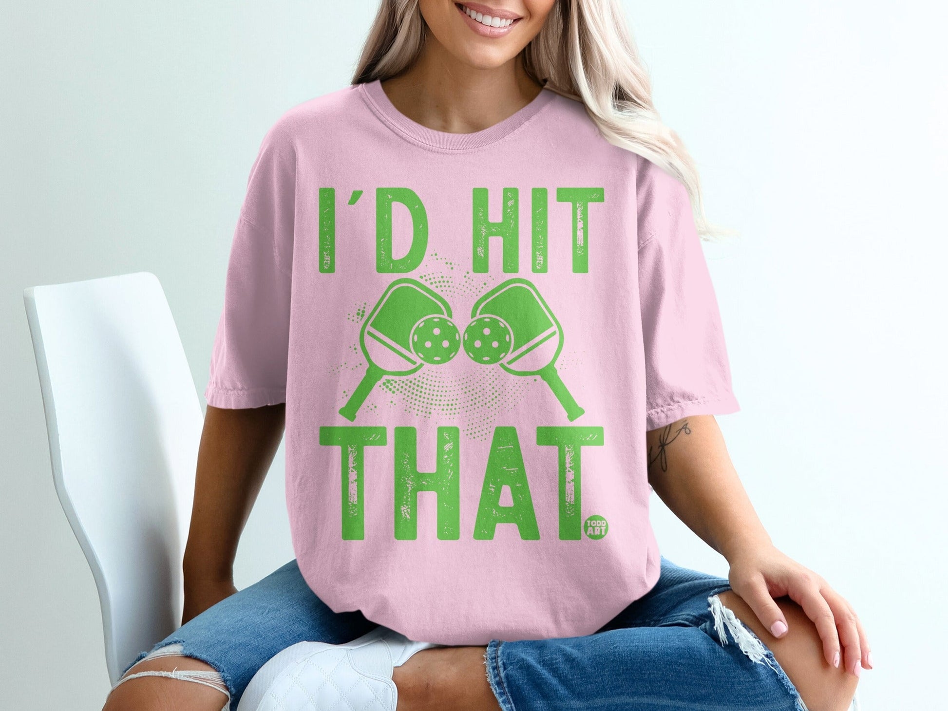Pink t-shirt with green graphic of pickleballs and paddles saying "I'd Hit That."