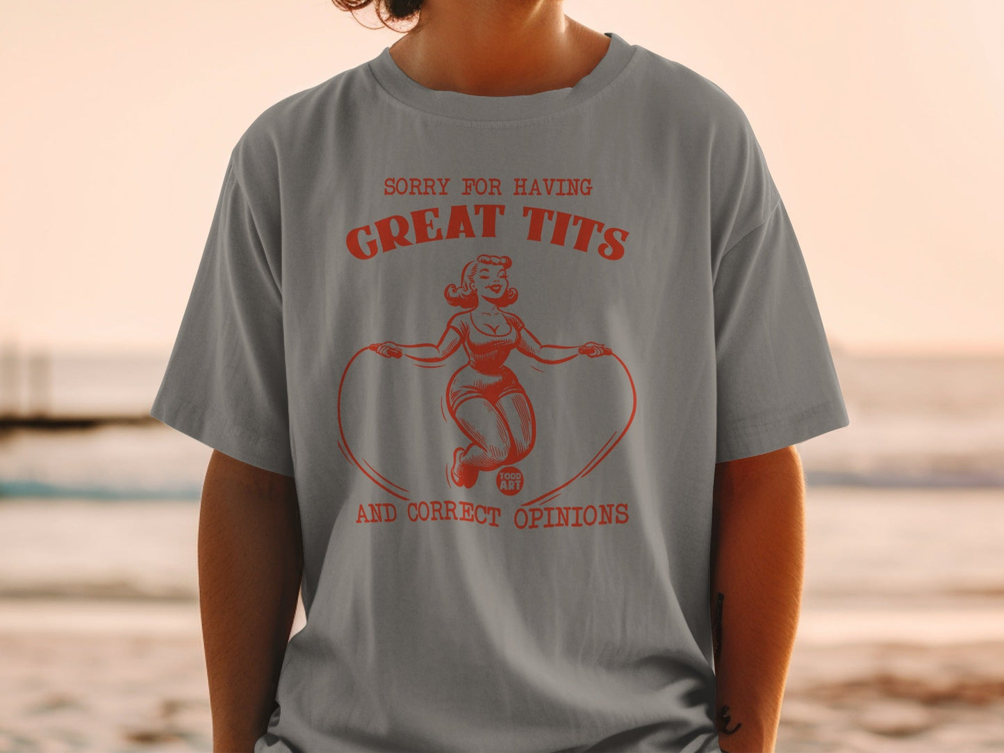 Gray t-shirt with red graphic of woman jumping rope, text "SORRY FOR HAVING GREAT TITS AND CORRECT OPINIONS".