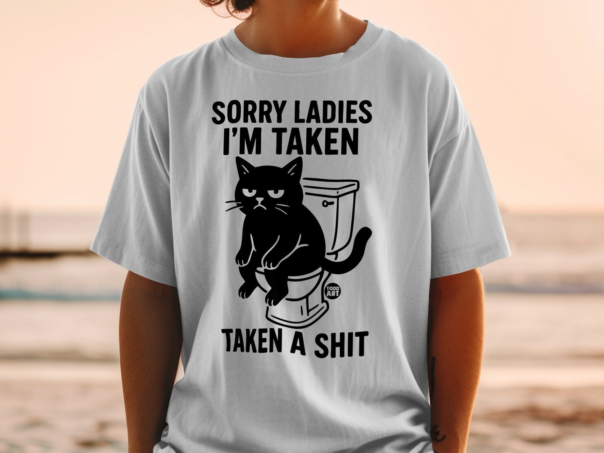 T-shirt with black graphic of a cat on a toilet, text reads "SORRY LADIES I'M TAKEN", "TAKEN A SHIT".