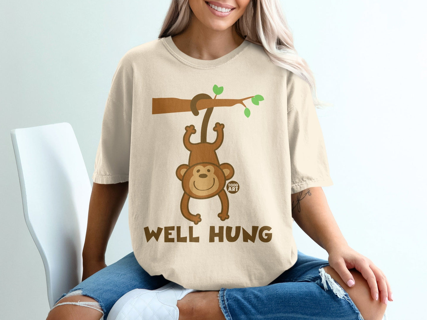 Woman wearing a beige t-shirt with a cartoon monkey hanging from a branch.