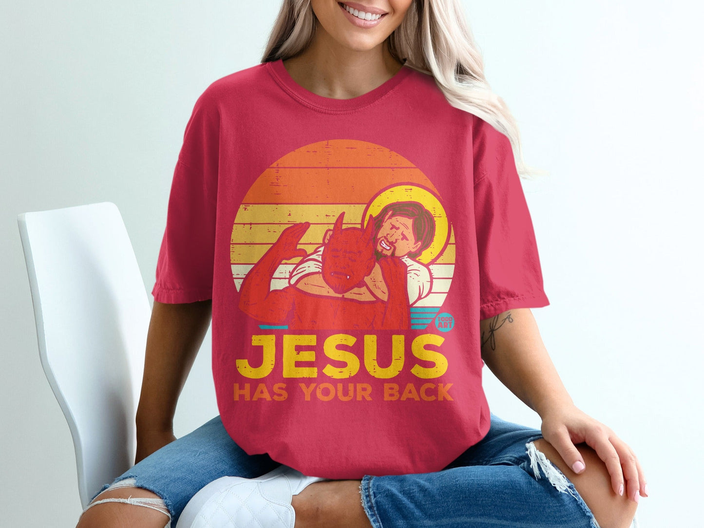 Red t-shirt with graphic of Jesus and devil and text "JESUS HAS YOUR BACK".