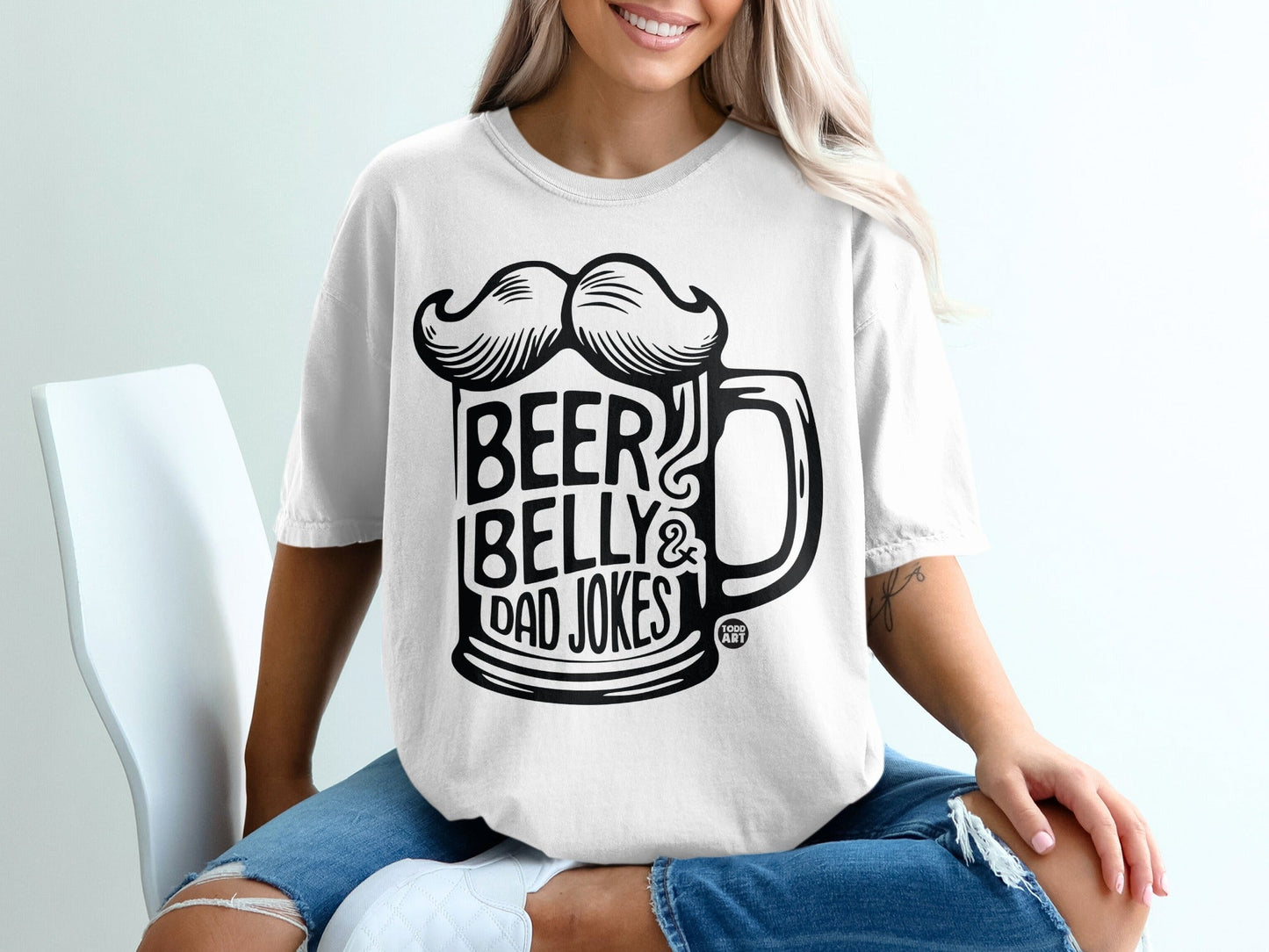 White t-shirt with black graphic of a beer mug with a mustache, reading "BEER BELLY & DAD JOKES".