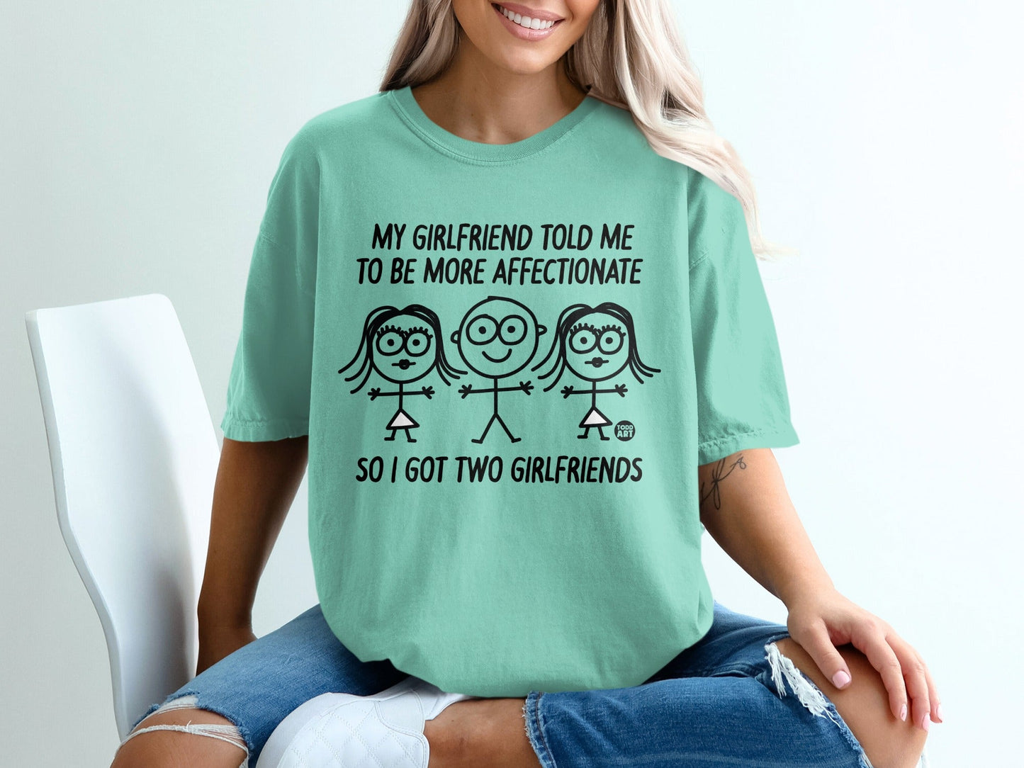 Mint t-shirt with cartoon figures and text "My girlfriend told me to be more affectionate so I got two girlfriends."