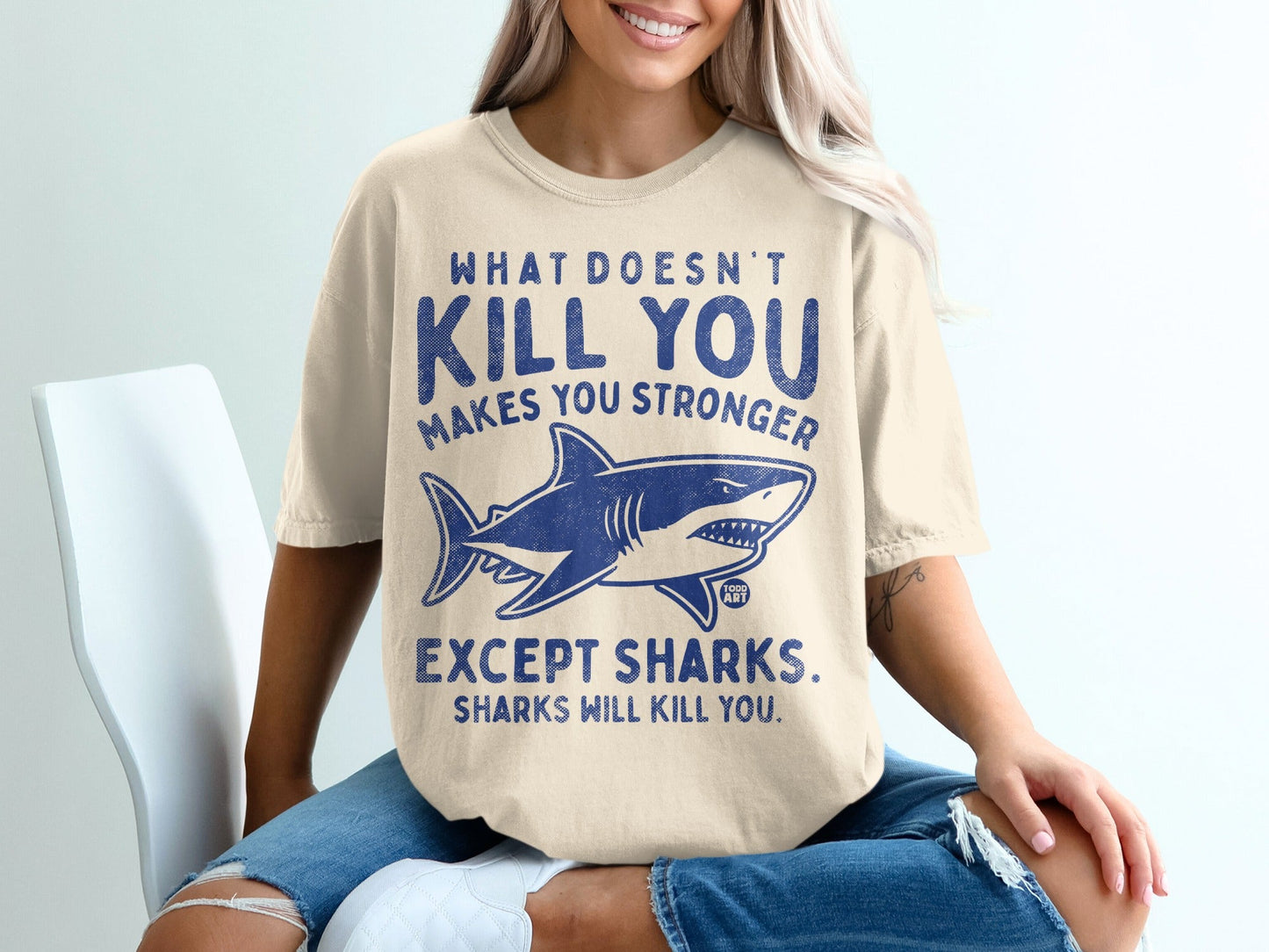 T-shirt with shark graphic and text "What doesn't kill you makes you stronger, except sharks. Sharks will kill you."