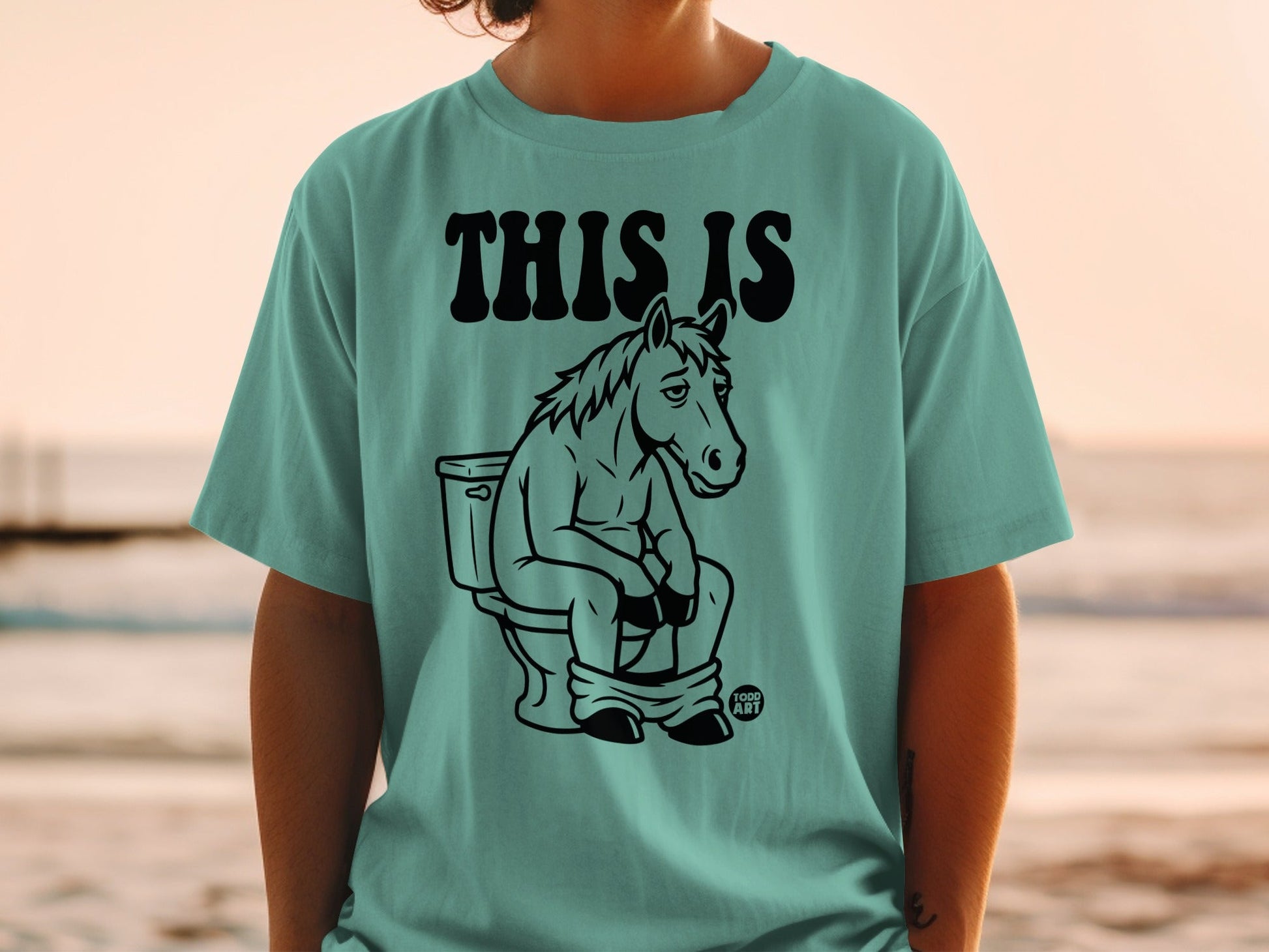 T-shirt with text "THIS IS" and illustration of a horse sitting on a toilet.