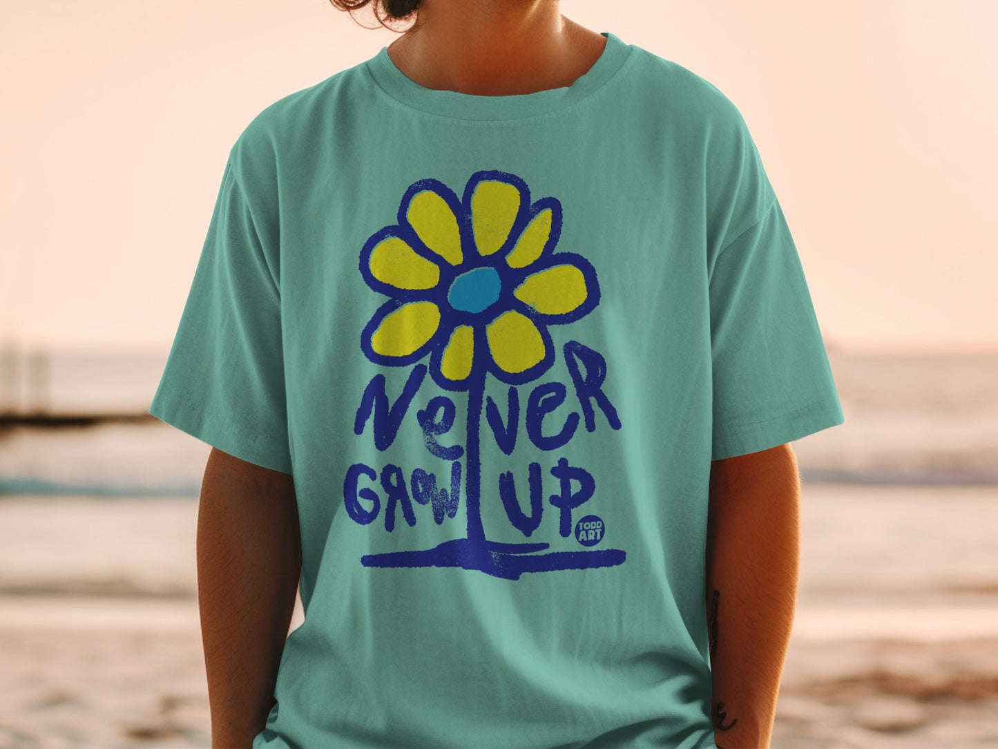 Teal t-shirt with "Never Grow Up" and a yellow flower graphic.