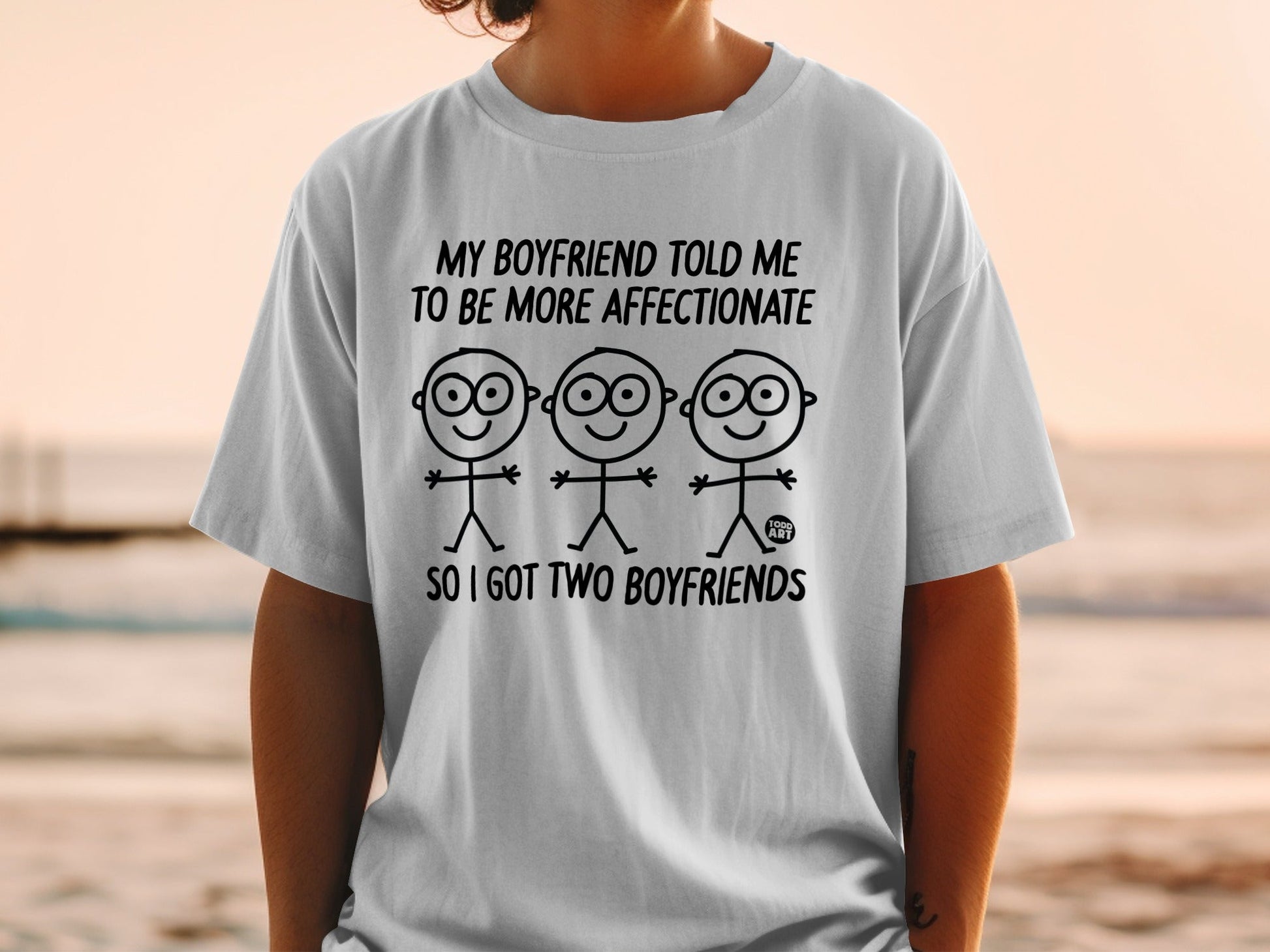 White t-shirt with "My boyfriend told me to be more affectionate so I got two boyfriends" text and stick figures.