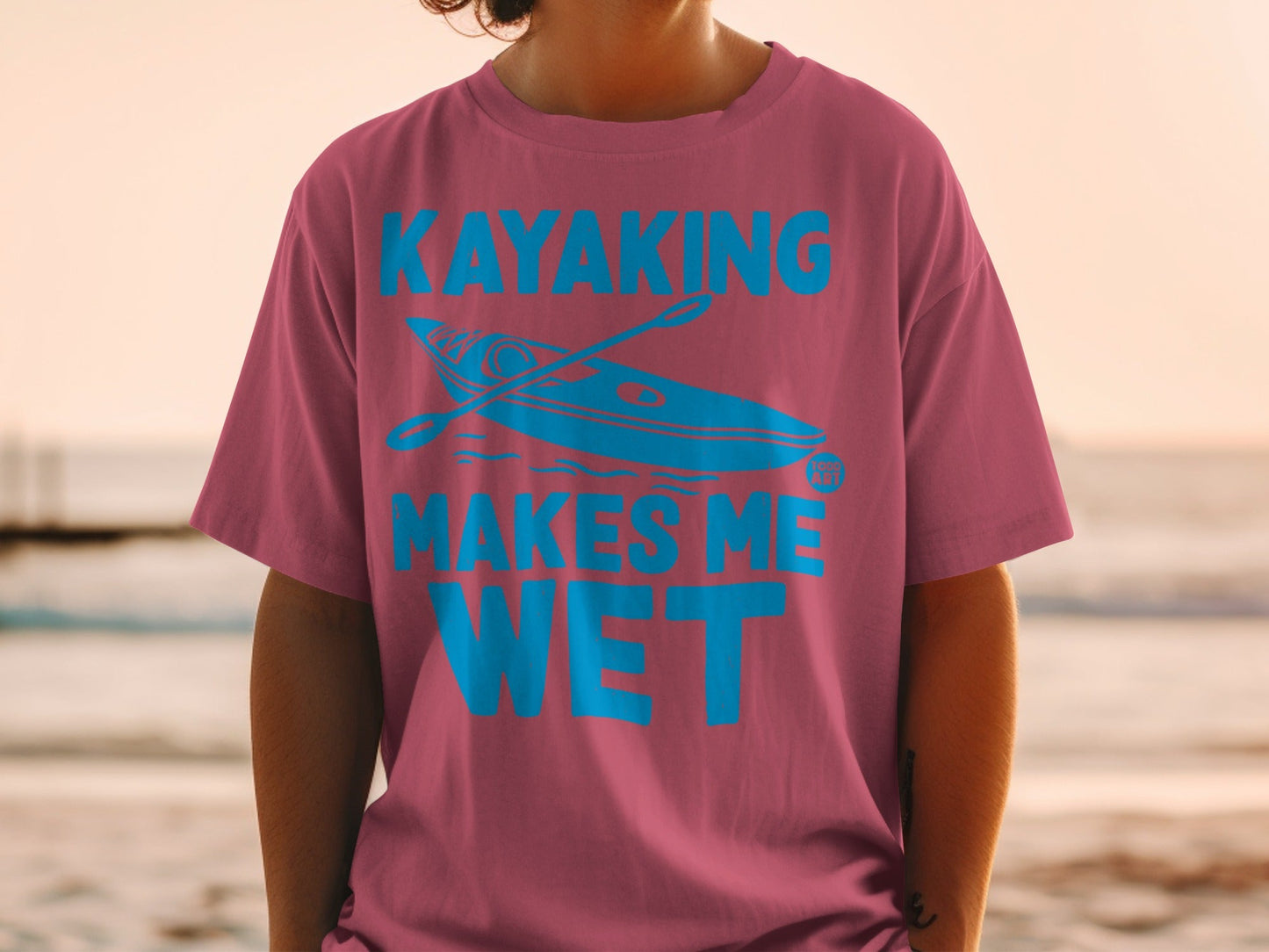 Teal kayak graphic with text "KAYAKING MAKES ME WET" on a pink t-shirt.