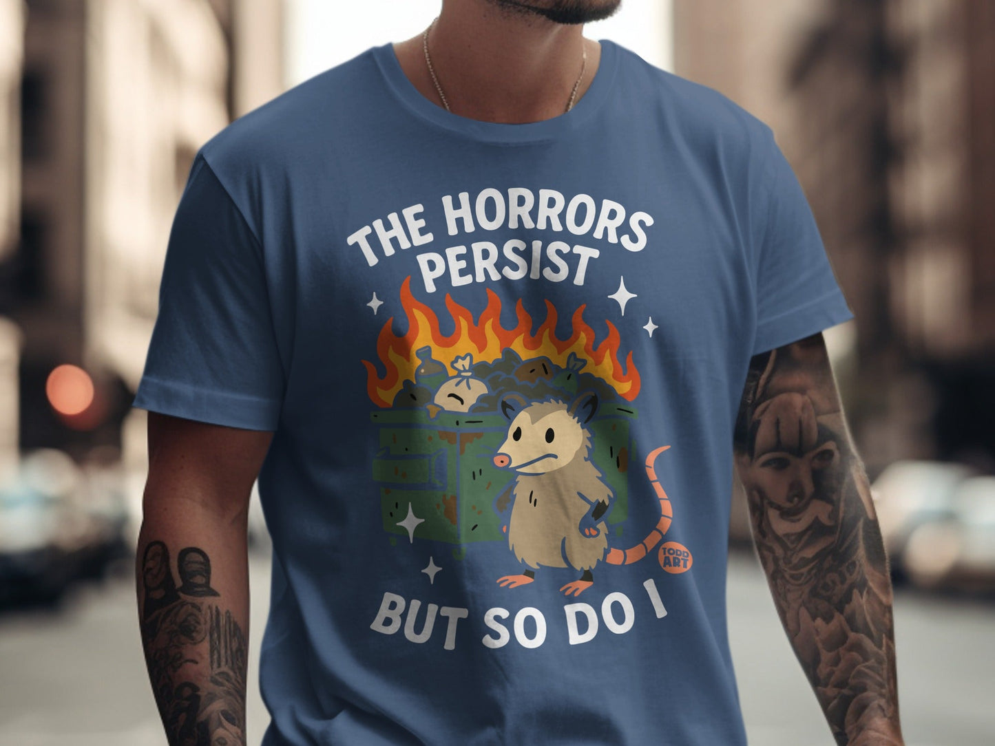T-shirt with opossum and burning trash, text reads "The Horrors Persist But So Do I".