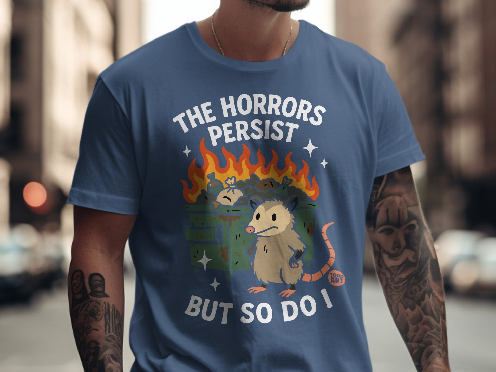 T-shirt with opossum and burning trash, text reads "The Horrors Persist But So Do I".