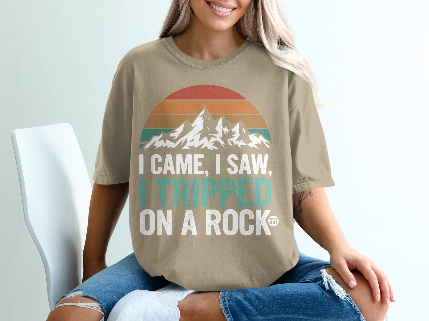 Tan t-shirt with mountains and sunset graphic: "I came, I saw, I tripped on a rock."