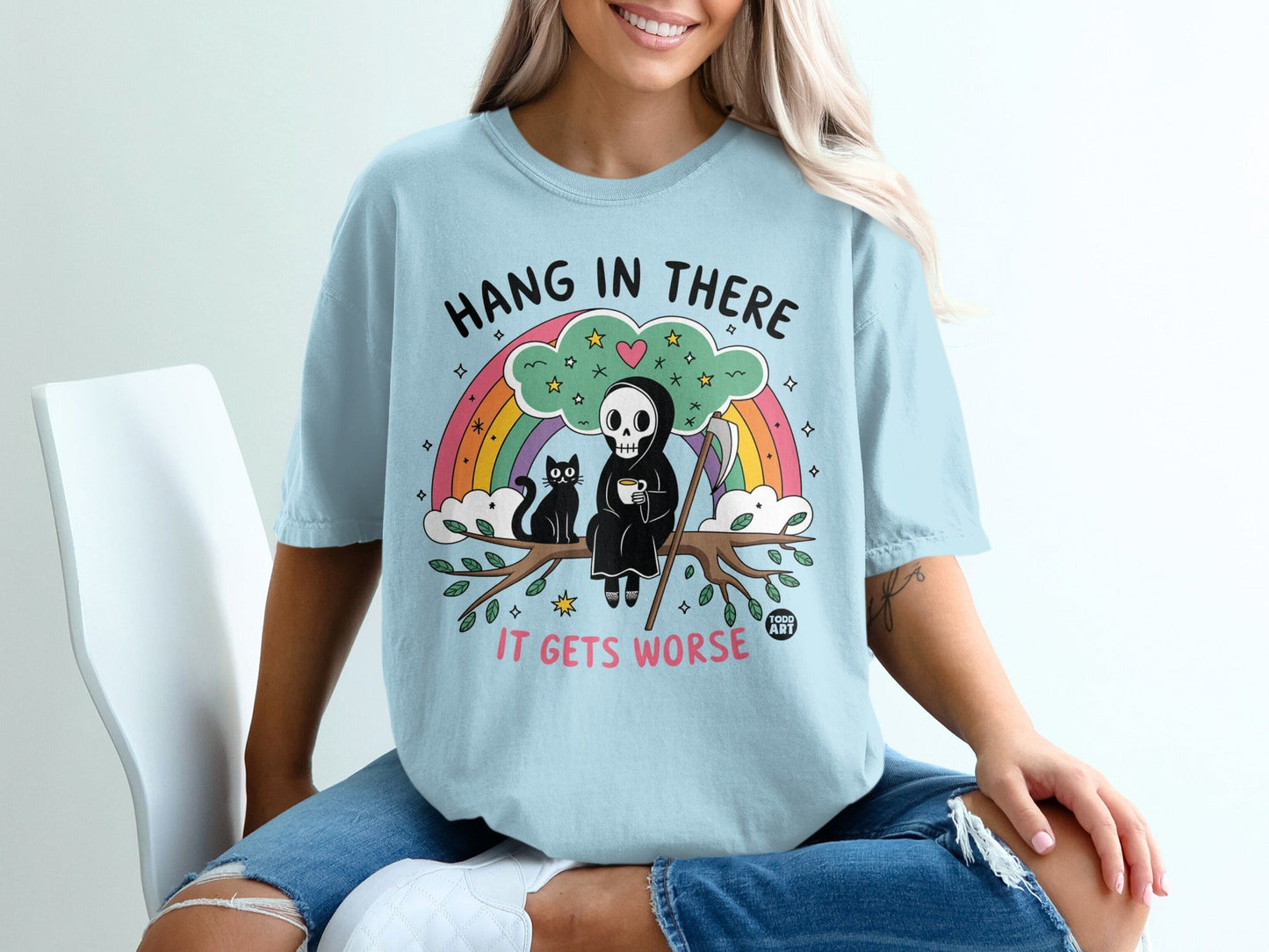 Light blue t-shirt with Grim Reaper, cat, coffee, and rainbow graphic.