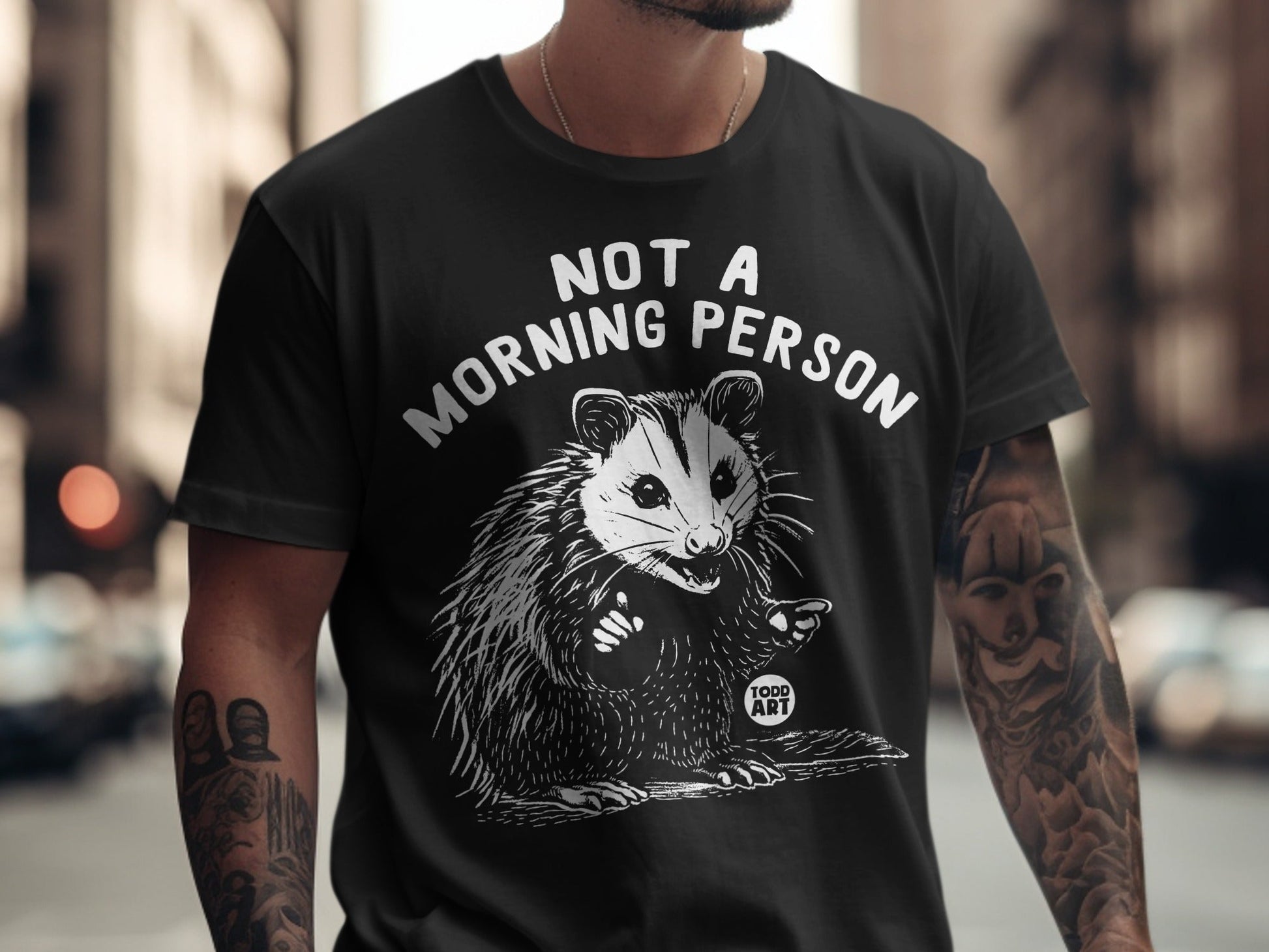Black t-shirt with white illustration of a opossum and text "NOT A MORNING PERSON".