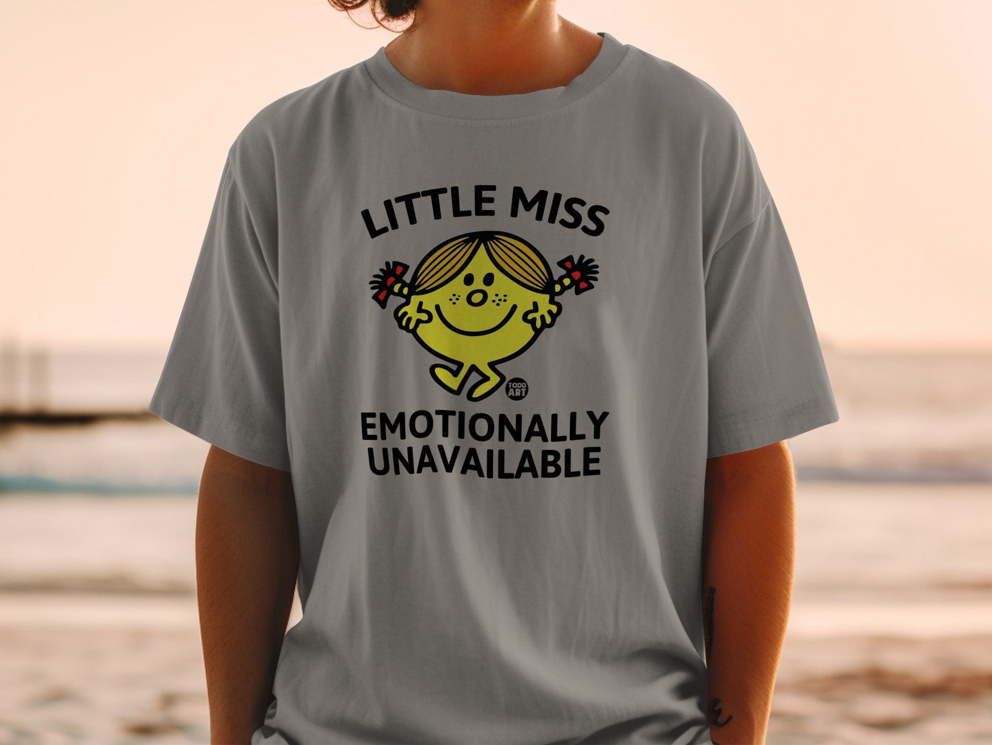 Little Miss Emotionally Unavailable graphic tee with character and text.
