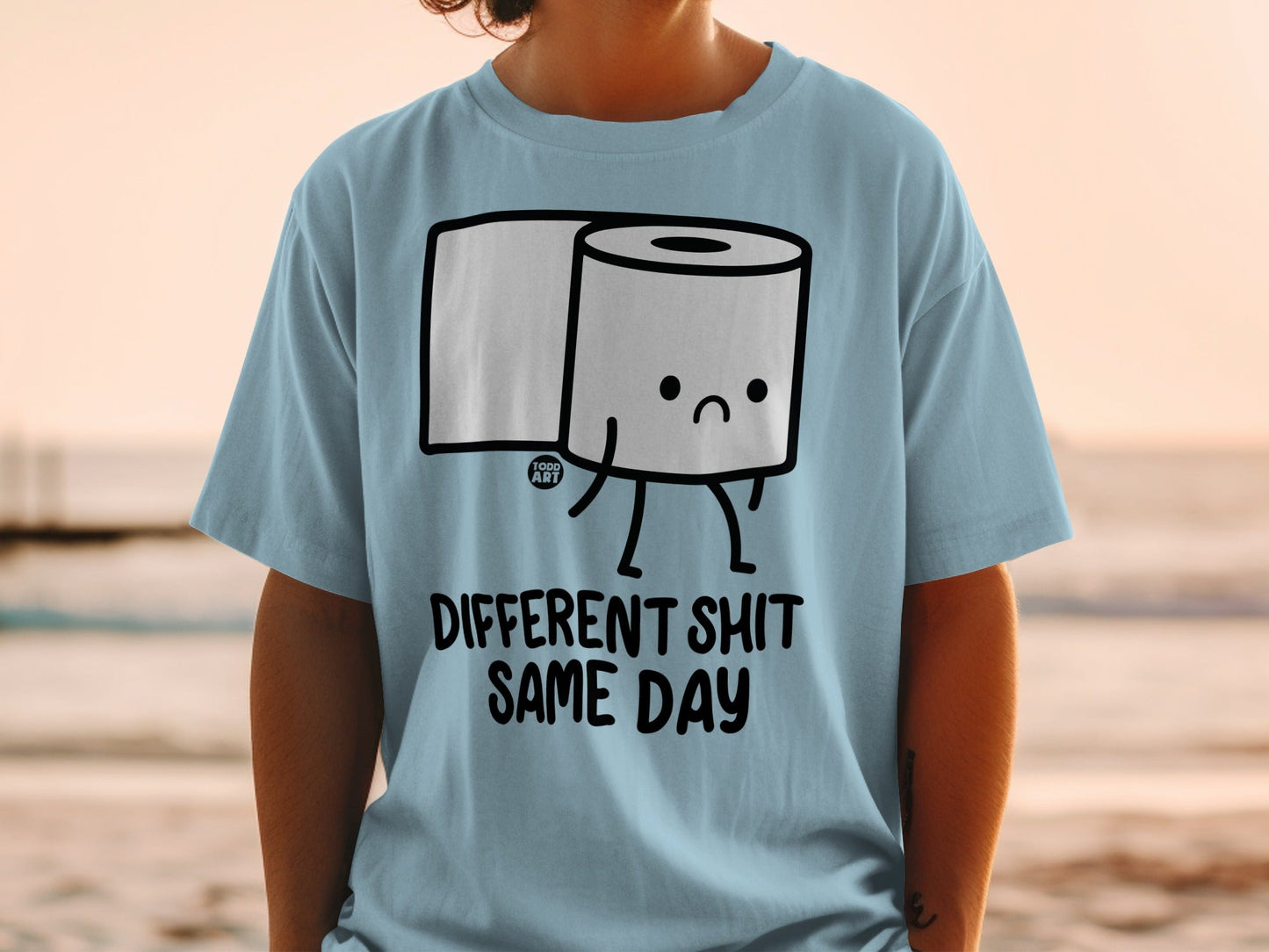 Light blue t-shirt with a cartoon toilet paper roll saying "DIFFERENT SHIT SAME DAY".