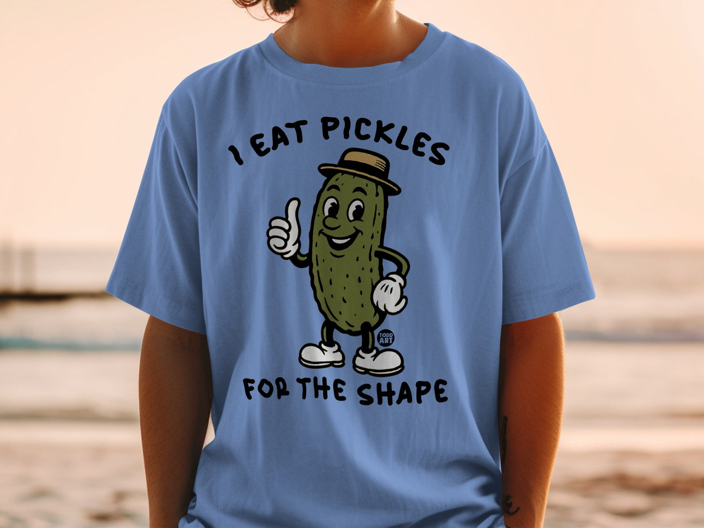 Cartoon pickle wearing a hat gives a thumbs up on a blue t-shirt.